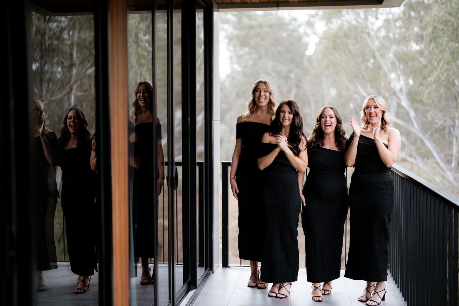 Bridesmaids in black dresses walking together in modern venue hallway.
