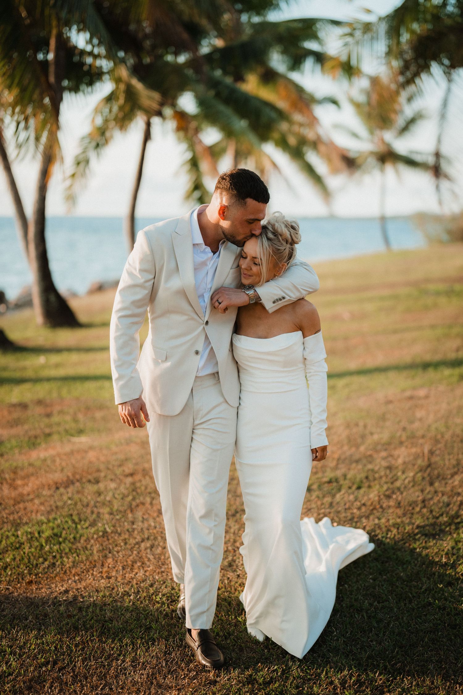 Romantic moment between newlyweds on a palm tree-lined beach at sunset.