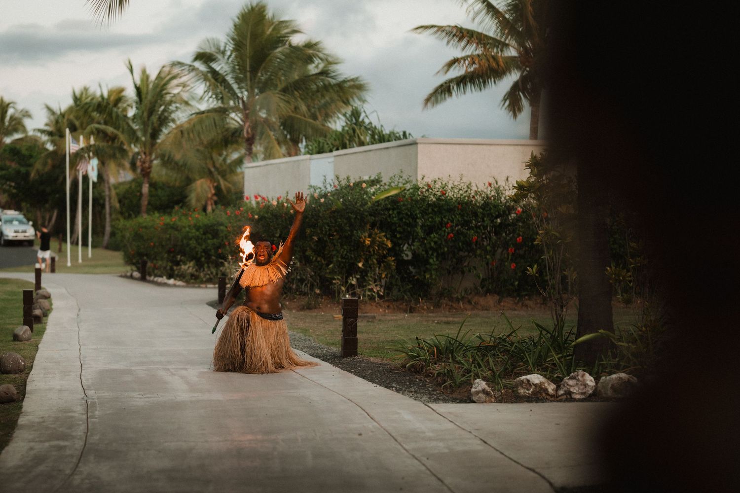Person in flowing dress dancing on palm-lined pathway at sunset.
