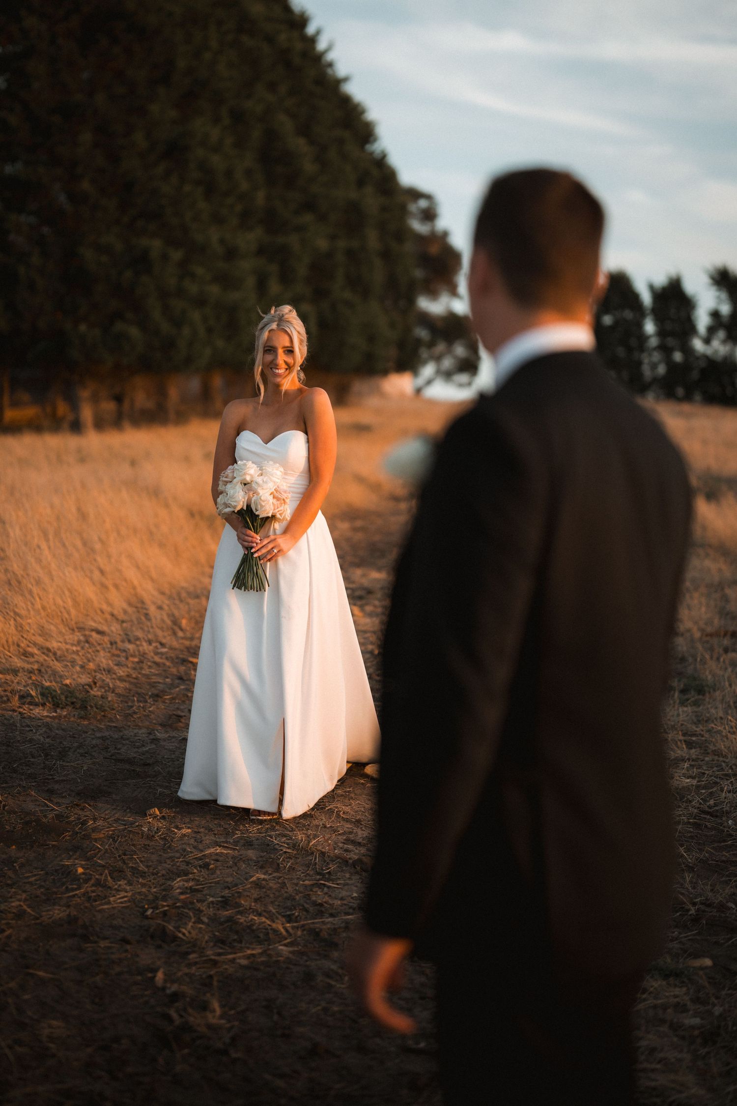 A sunset wedding portrait in a golden field with dramatic lighting and coastal backdrop.