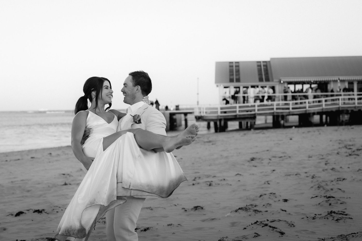 Black and white beach wedding portraits with pier in background.