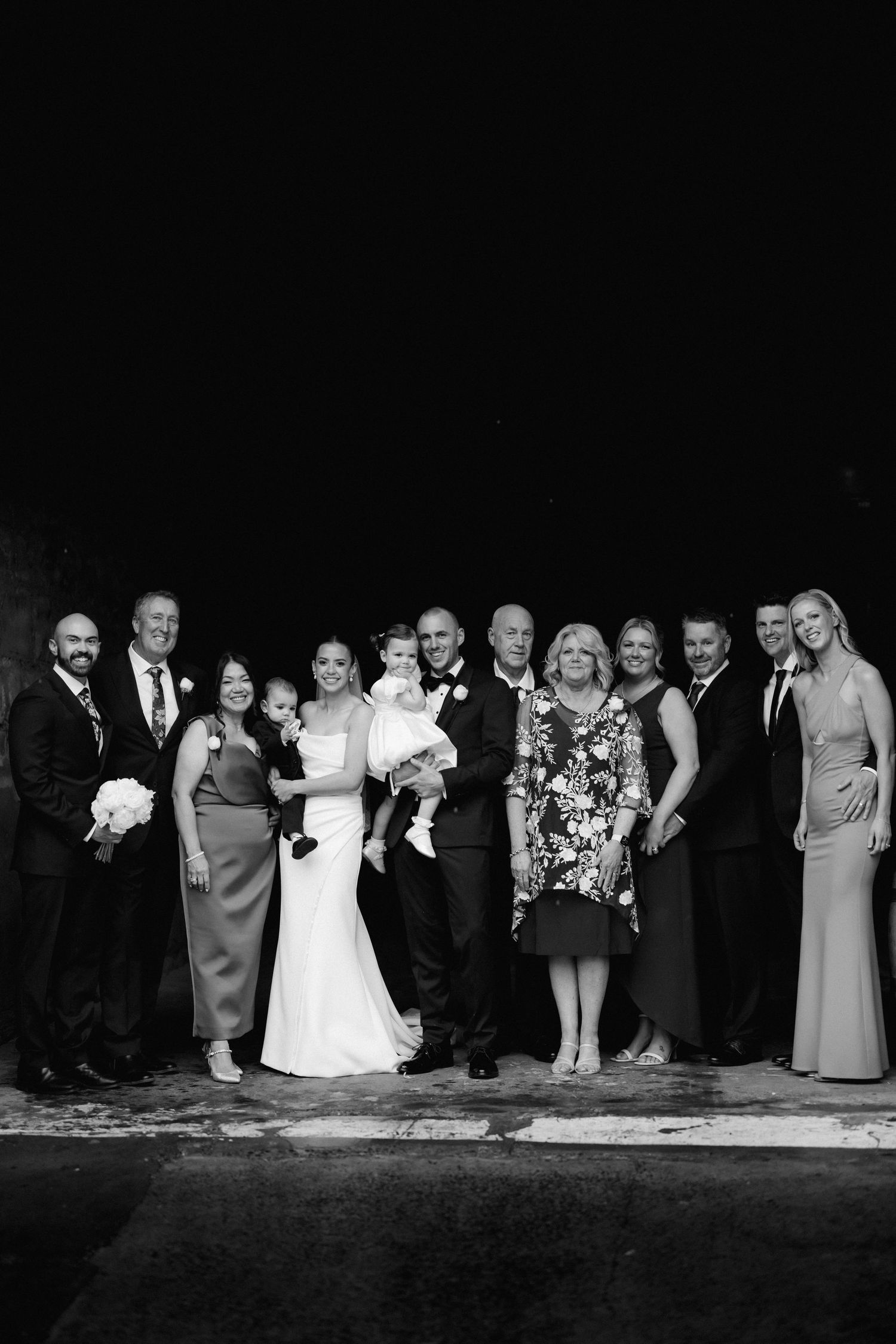 A formal black and white group photo of a wedding party lined up together.