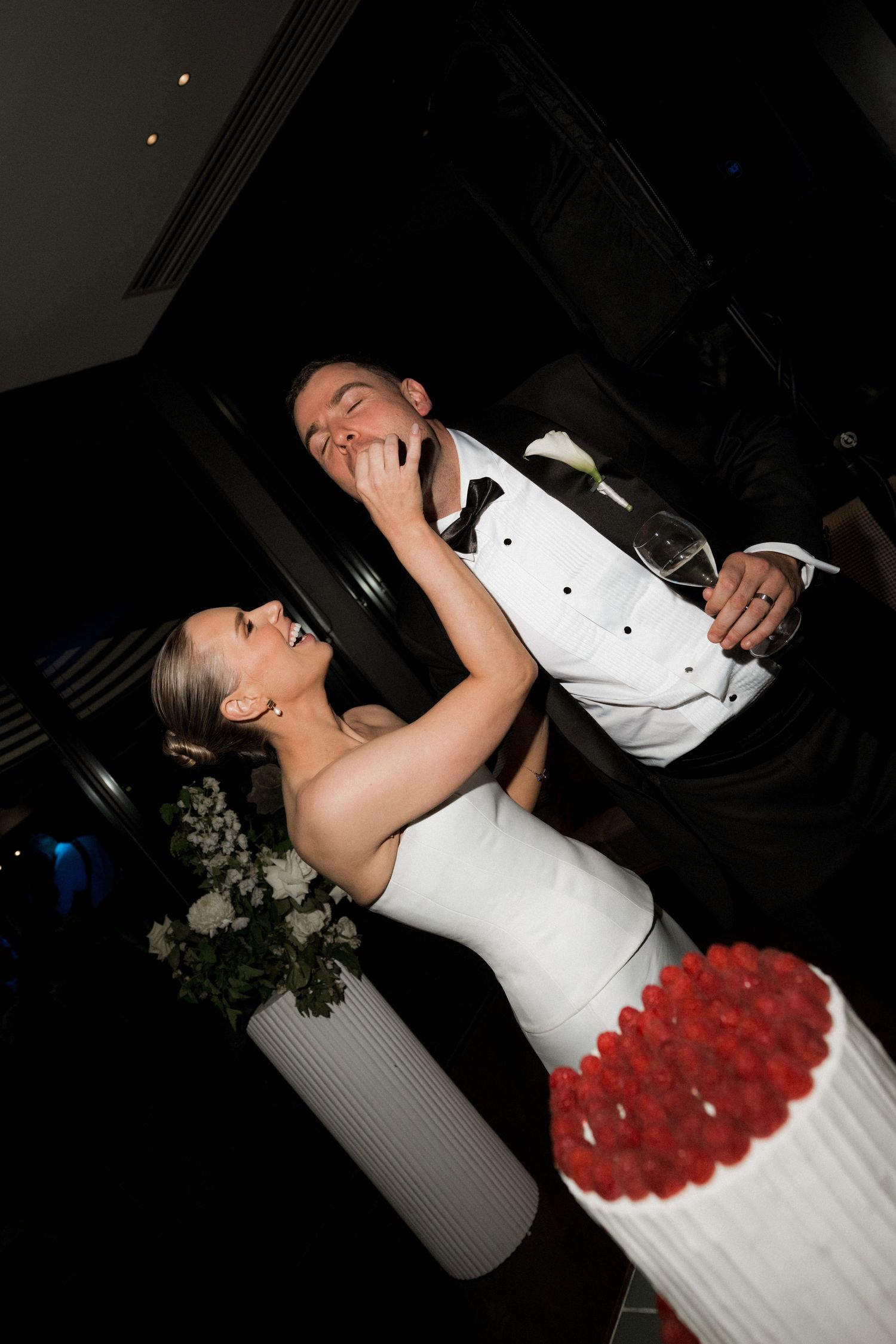 A bride in a white dress with red floral details dances at a dimly lit reception.