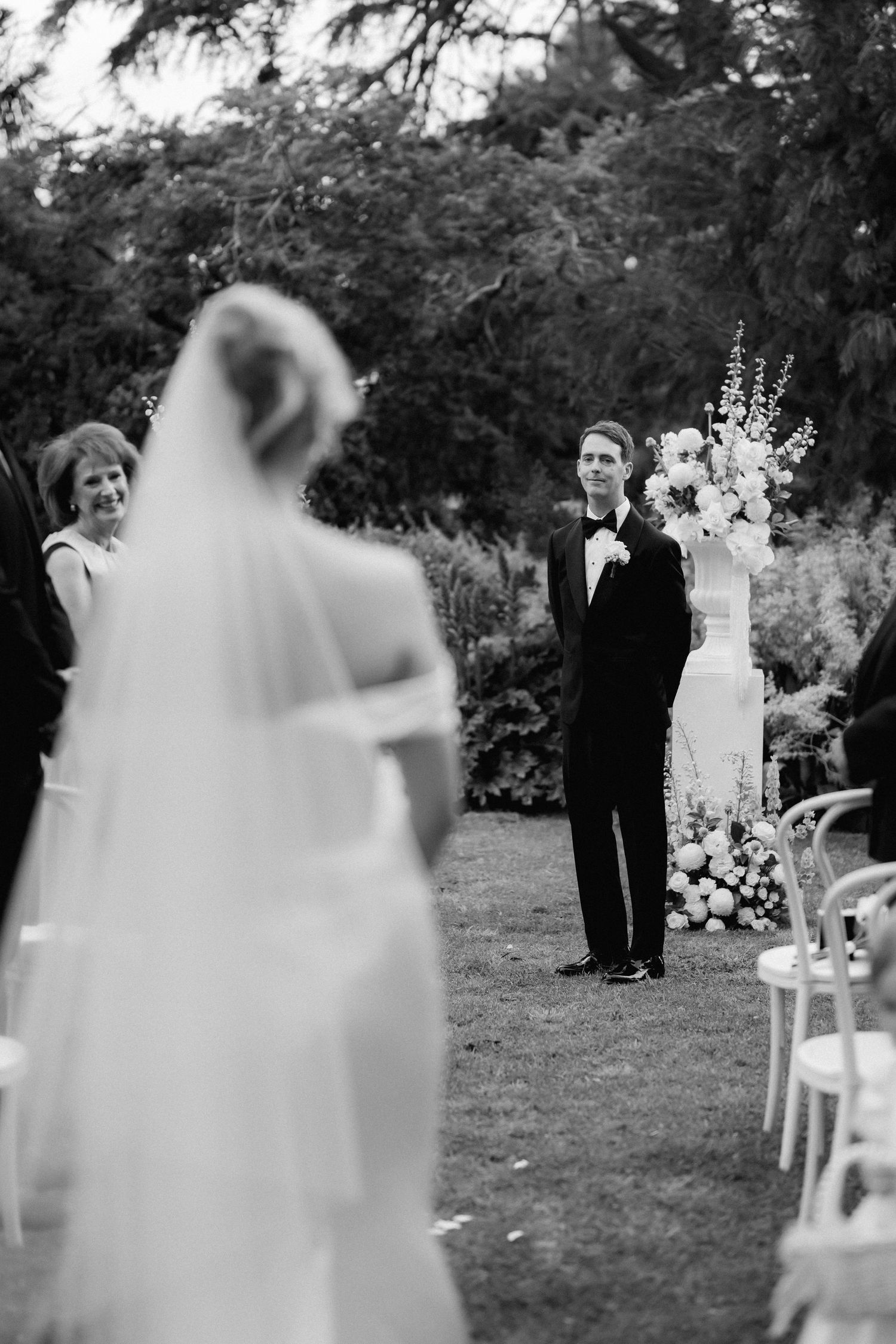 Wedding ceremony setup outdoors with white chairs and floral arrangements against a natural backdrop.