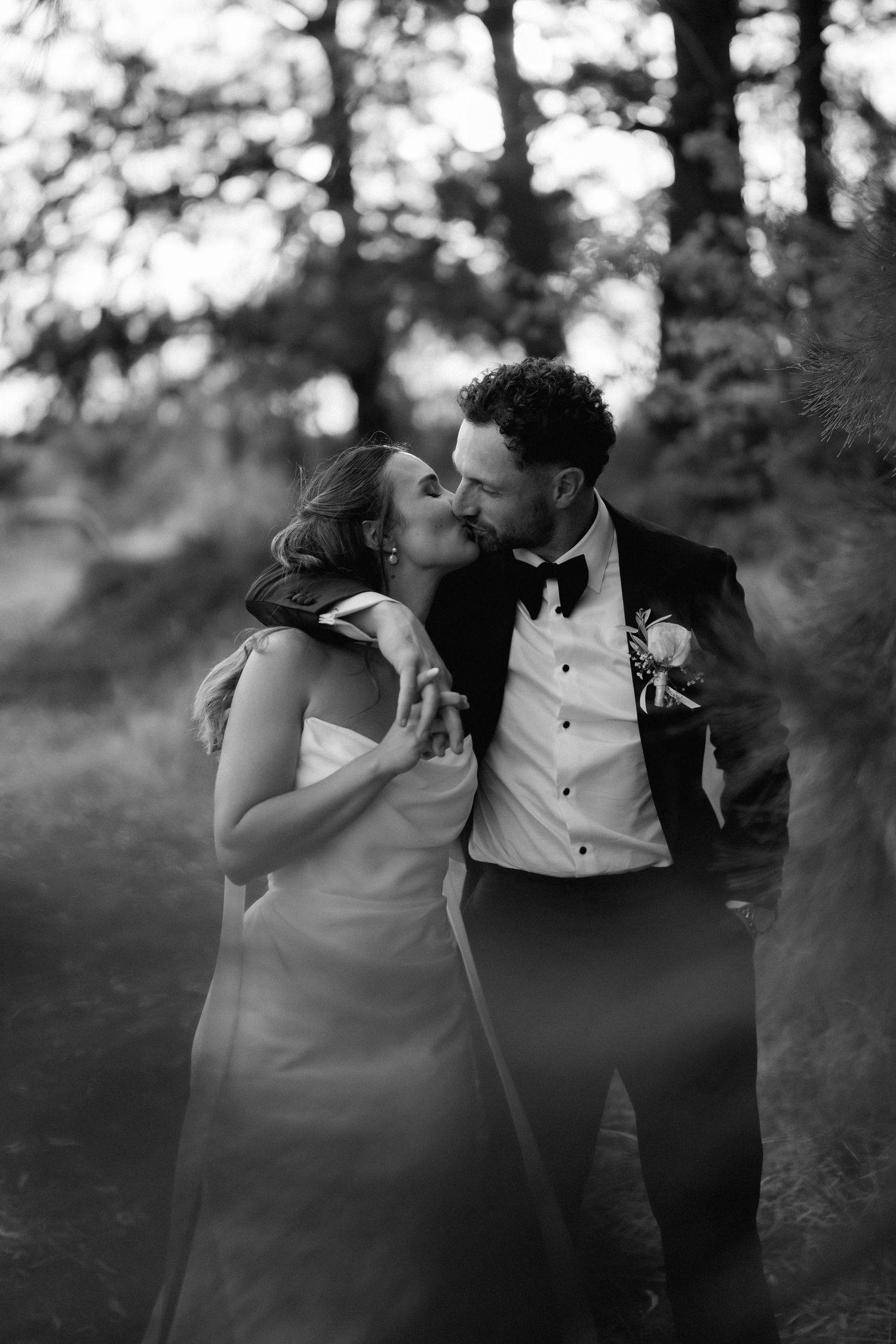 Intimate black and white portrait of newlyweds sharing a tender moment in a wooded setting.