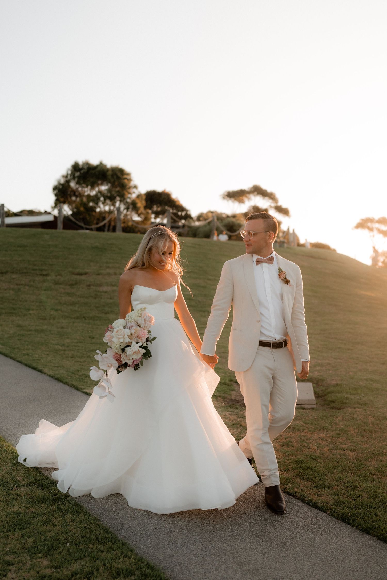A romantic sunset wedding photoshoot on a grassy hillside path.