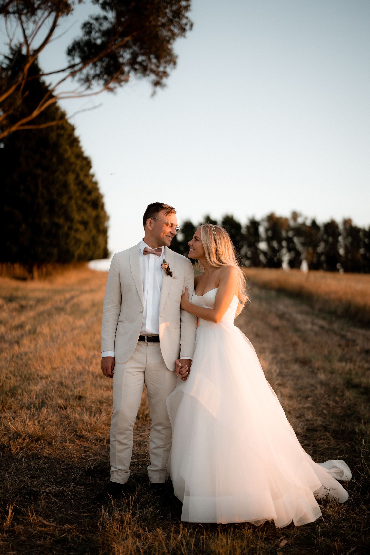 A couple in wedding attire walks along a scenic hilltop path at sunset.