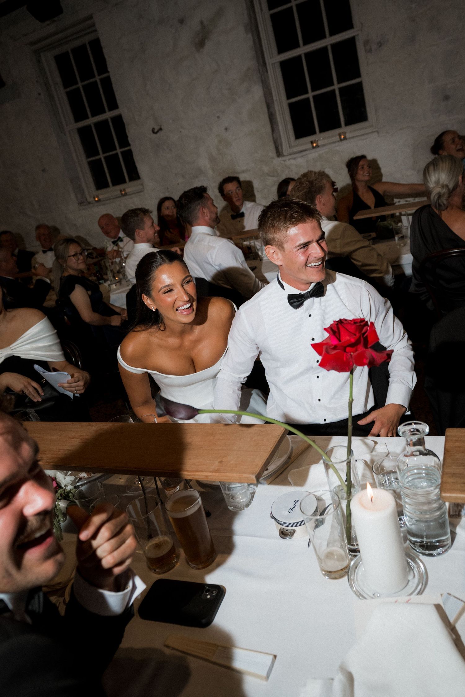 Wedding couple and guests share laughter during dinner reception at a rustic venue.