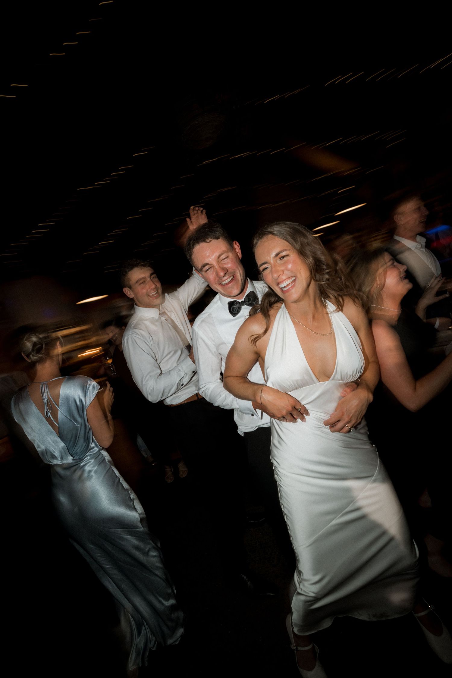 Wedding guests dancing and celebrating at a dimly lit reception venue.