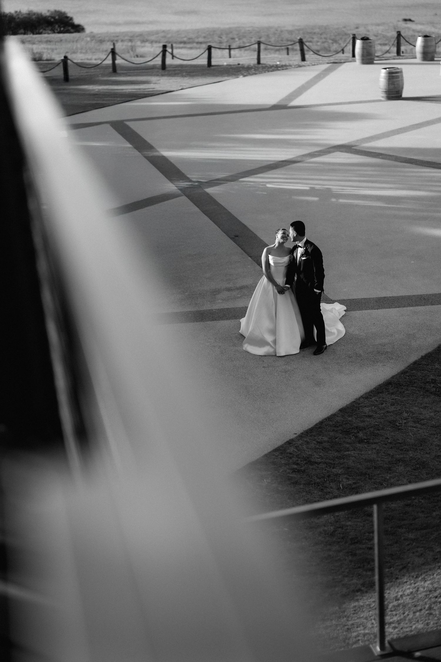 A couple in wedding attire shares an intimate moment on a paved terrace captured from above in black and white.