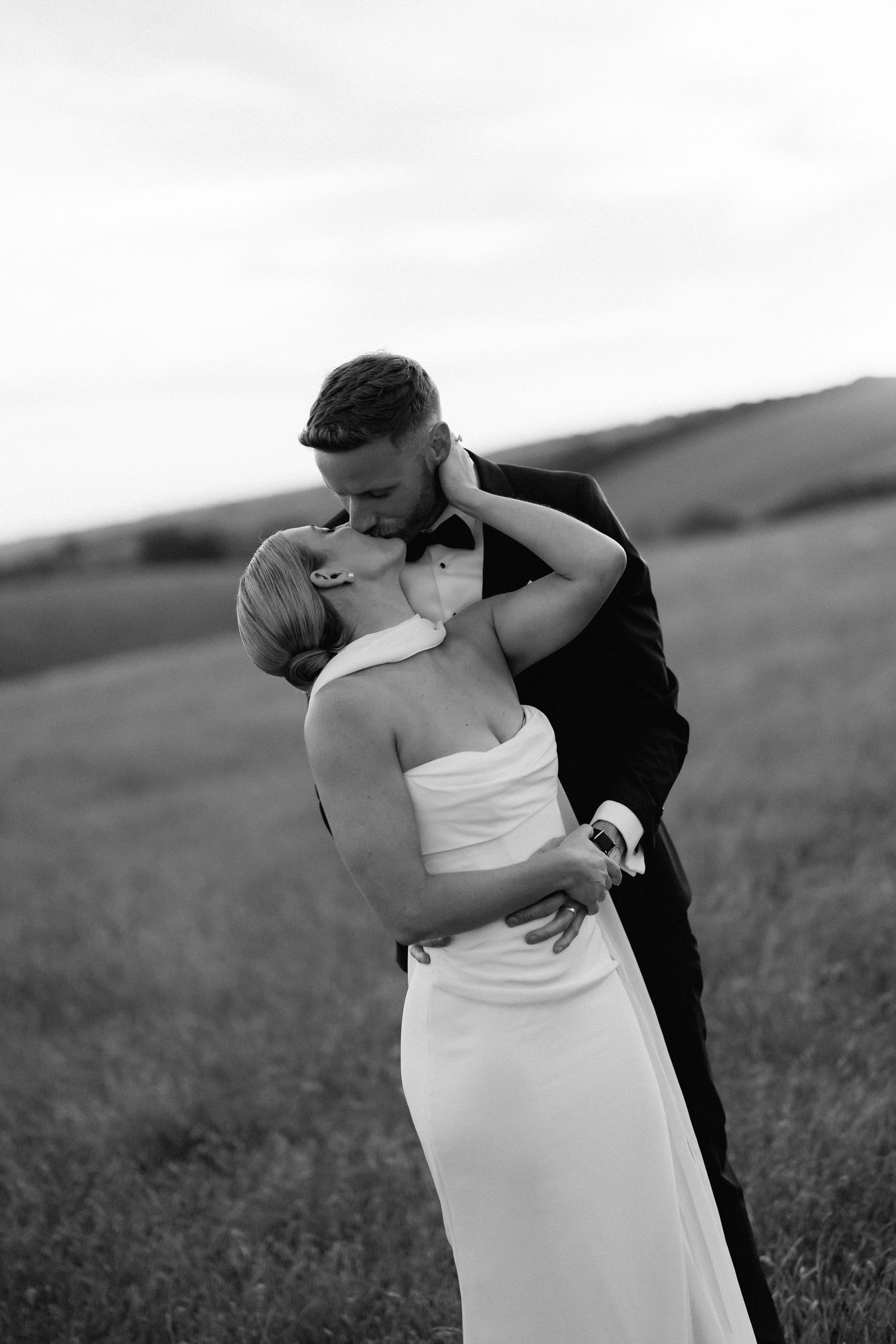 Black and white wedding photo series showing romantic embrace between couple in grassy field.