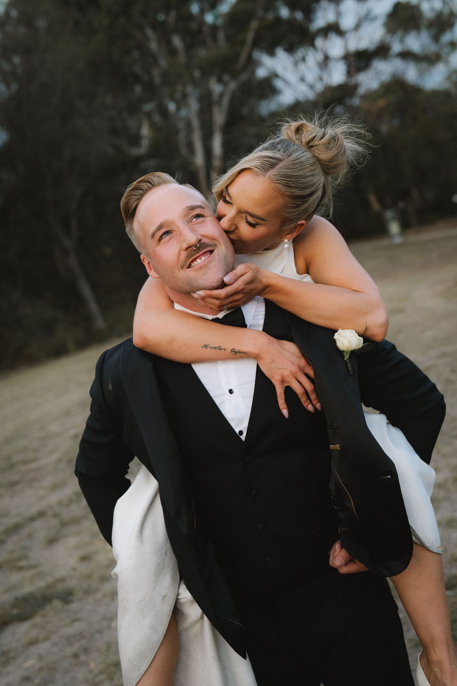 A couple shares playful and romantic moments during their wedding photoshoot outdoors with trees in the background.