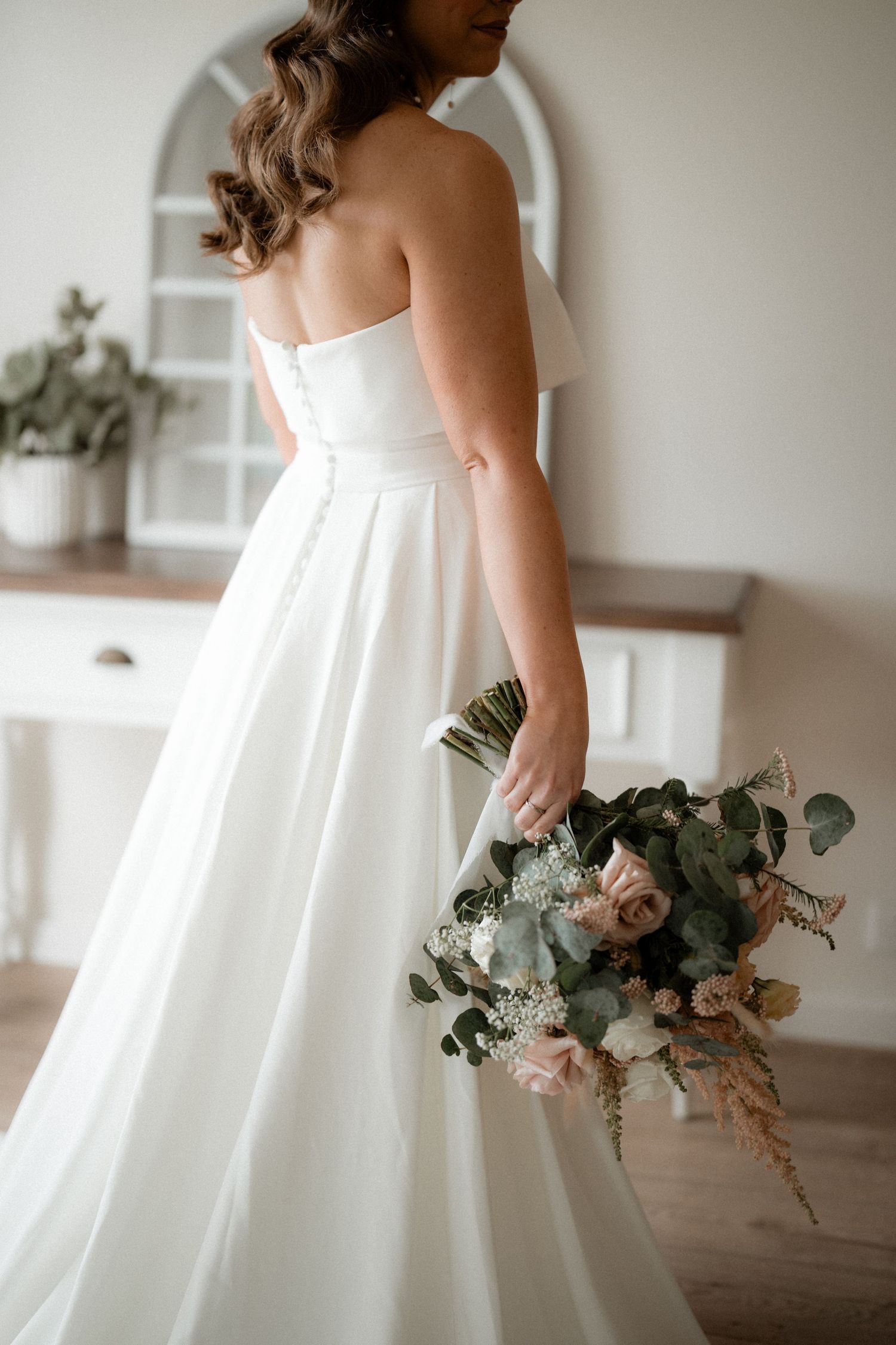 Elegant white wedding dress and bouquet with pink roses and eucalyptus captured in a bridal portrait.
