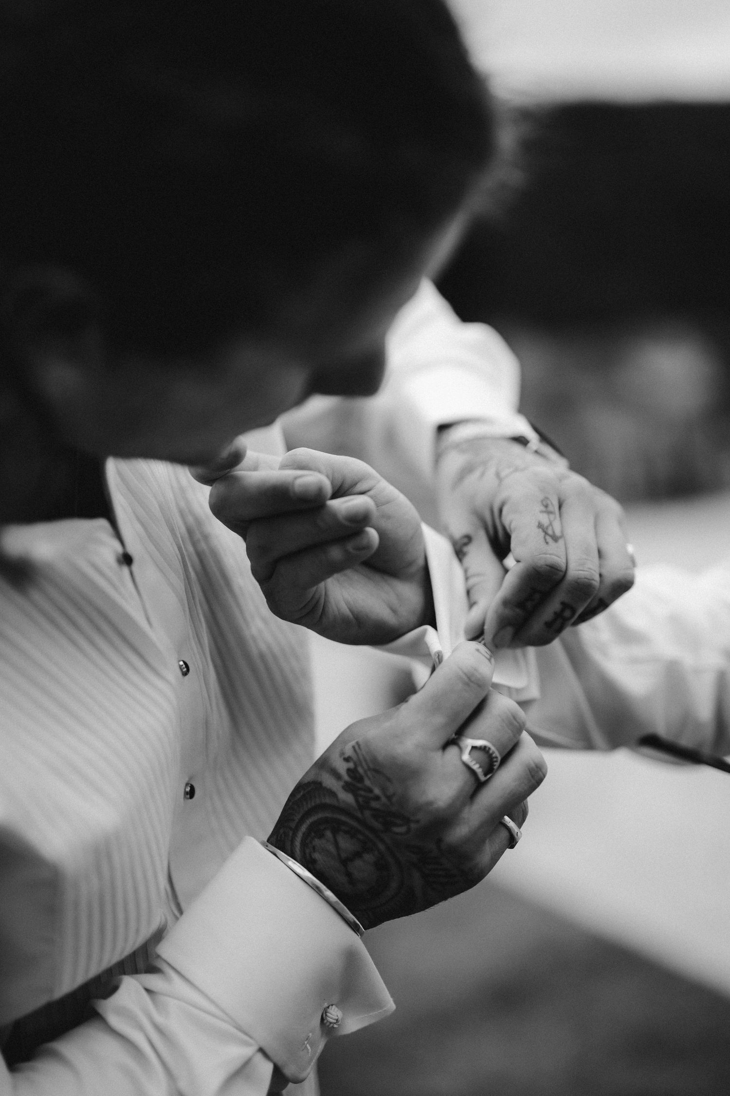 Close-up black and white photo showing hands buttoning up a sleeve cuff of a formal white dress shirt.