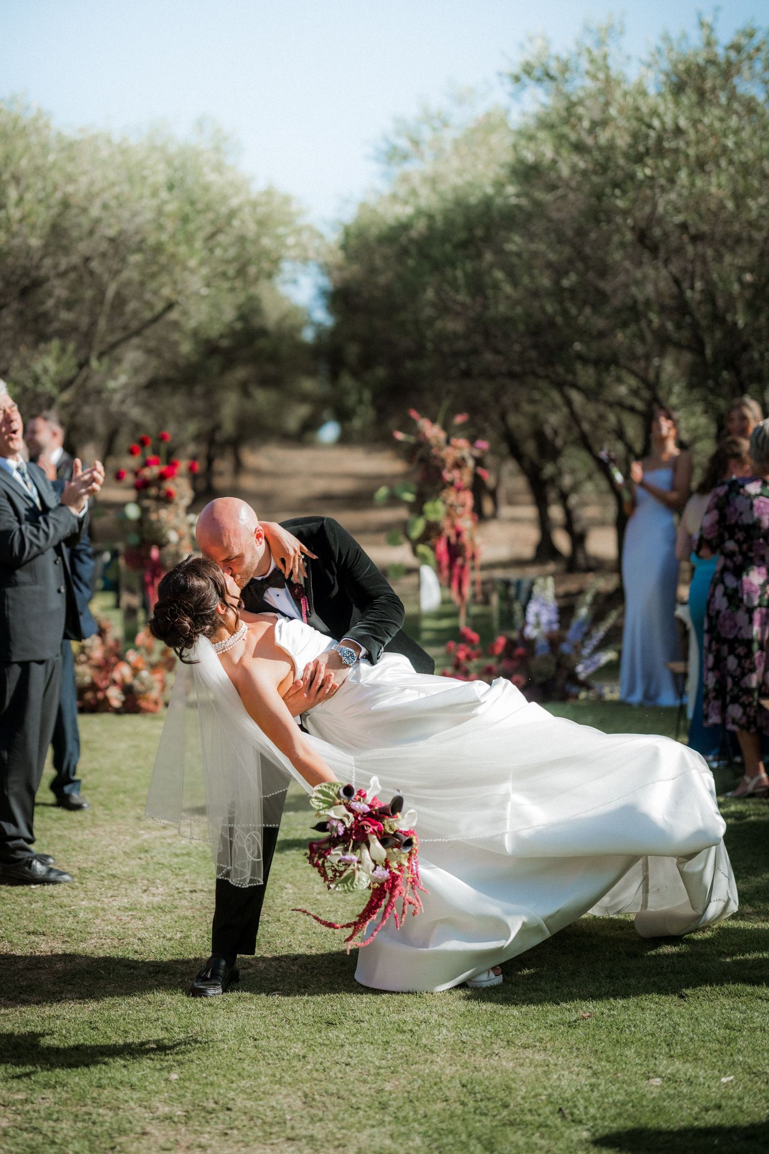 Dramatic dip pose during outdoor wedding ceremony surrounded by olive trees.