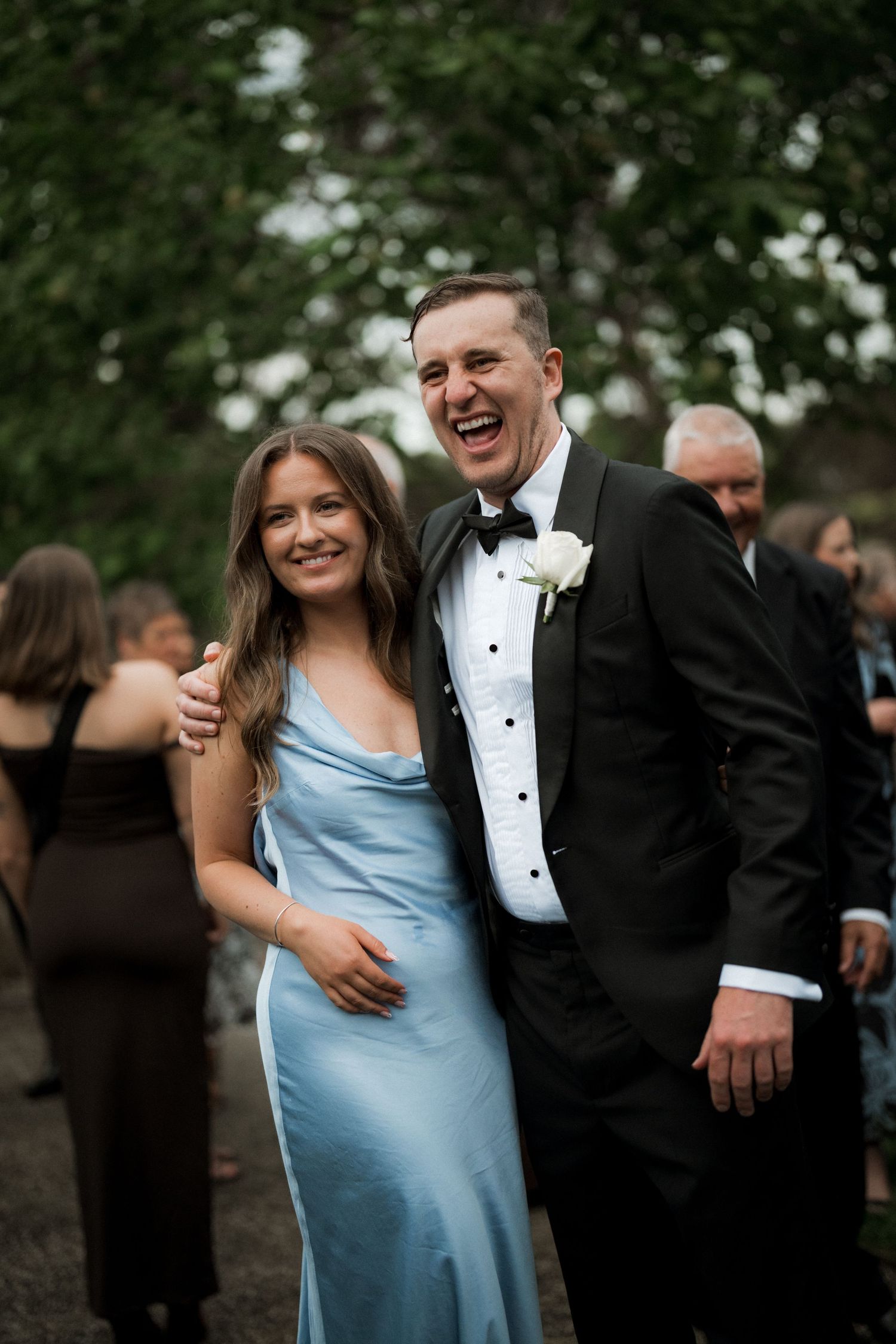 Wedding party members in formal attire share joyful moments outdoors.