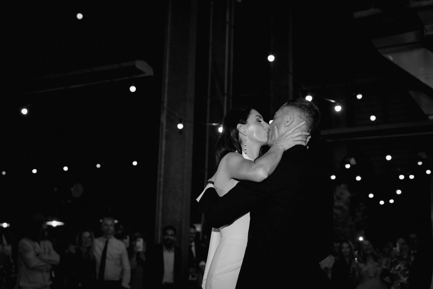A couple shares a romantic dance together at an indoor wedding reception with twinkling lights overhead.