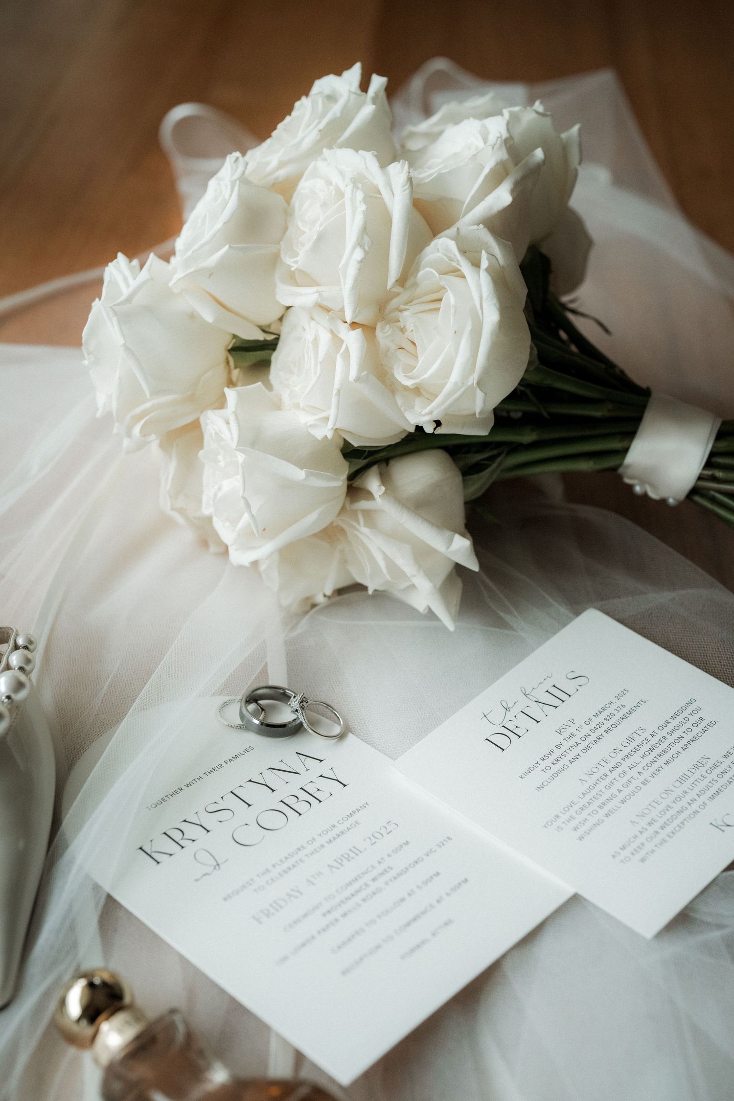 White wedding roses bouquet with rings and invitations on tulle fabric in elegant wedding day setting.