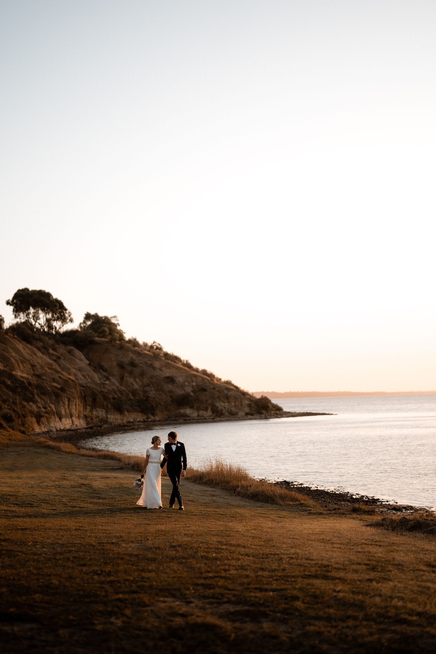 A couple walks along a coastal cliff path during golden hour with ocean views.