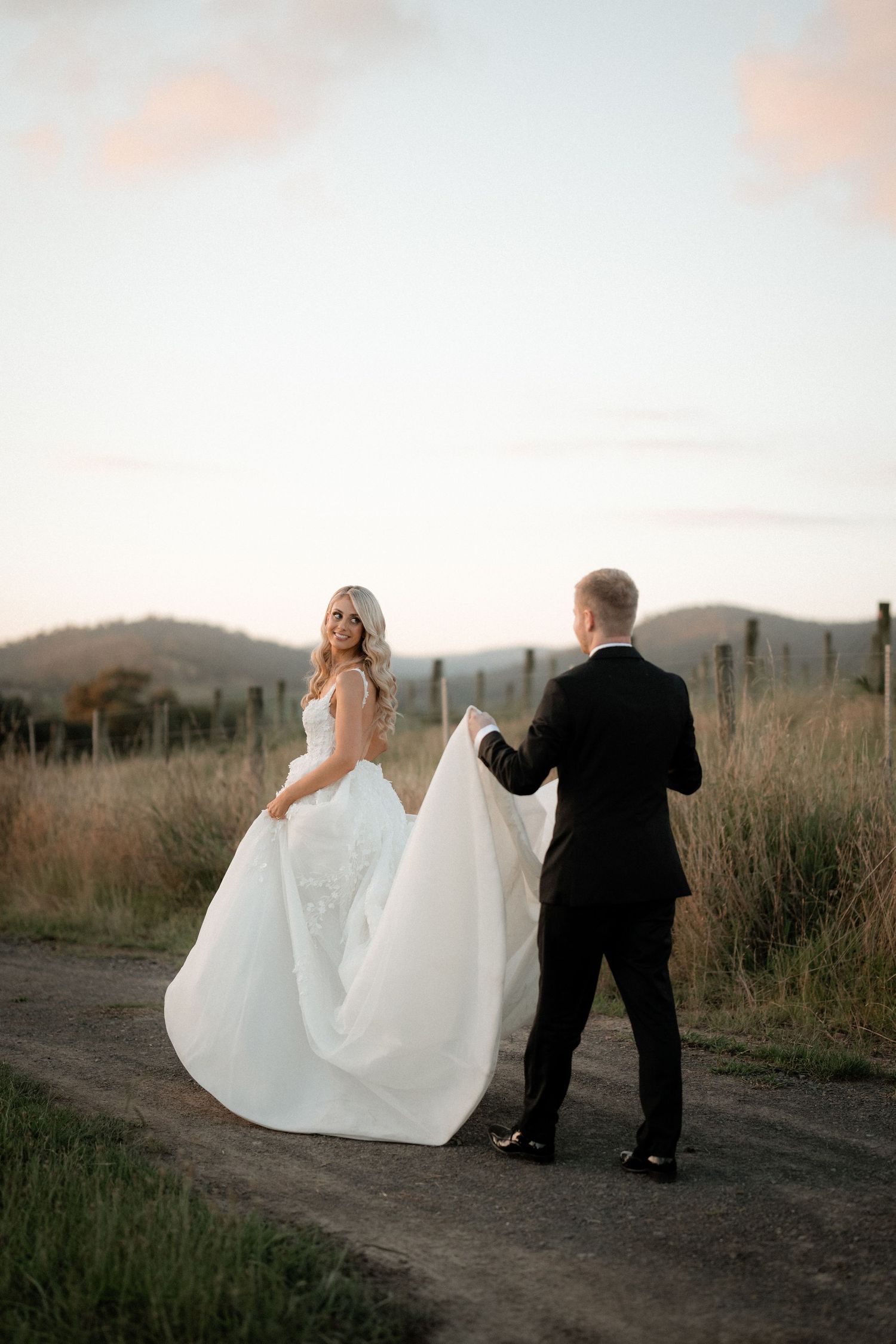 Sunset wedding photo of a couple on a dreamy countryside path with mountains in background.