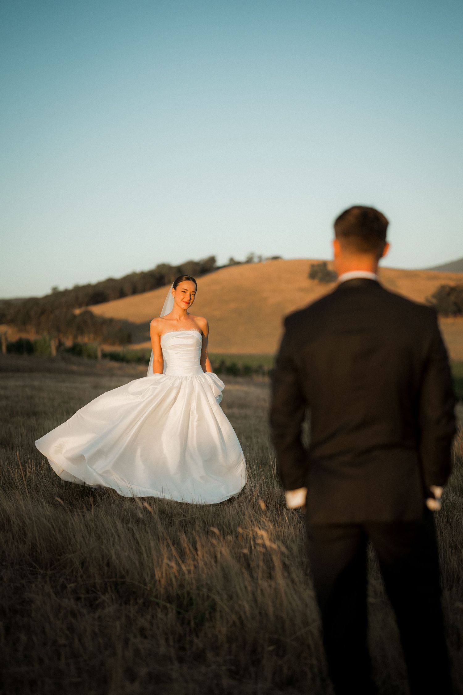 Wedding dress twirling in golden sunlight against rolling hills landscape.