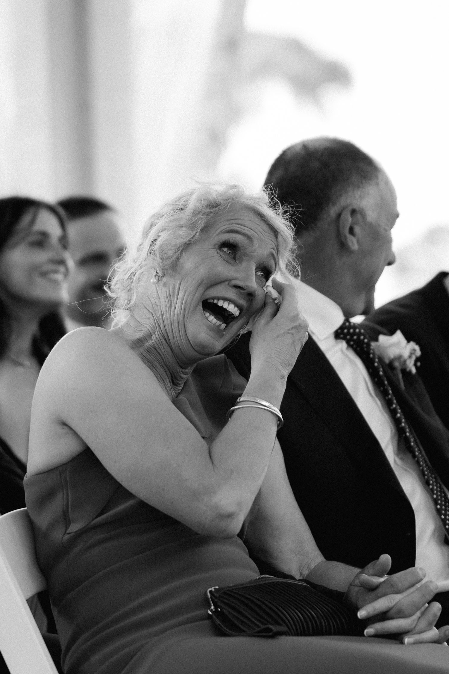 Black and white photos capture joyful laughter during an emotional wedding reception moment.