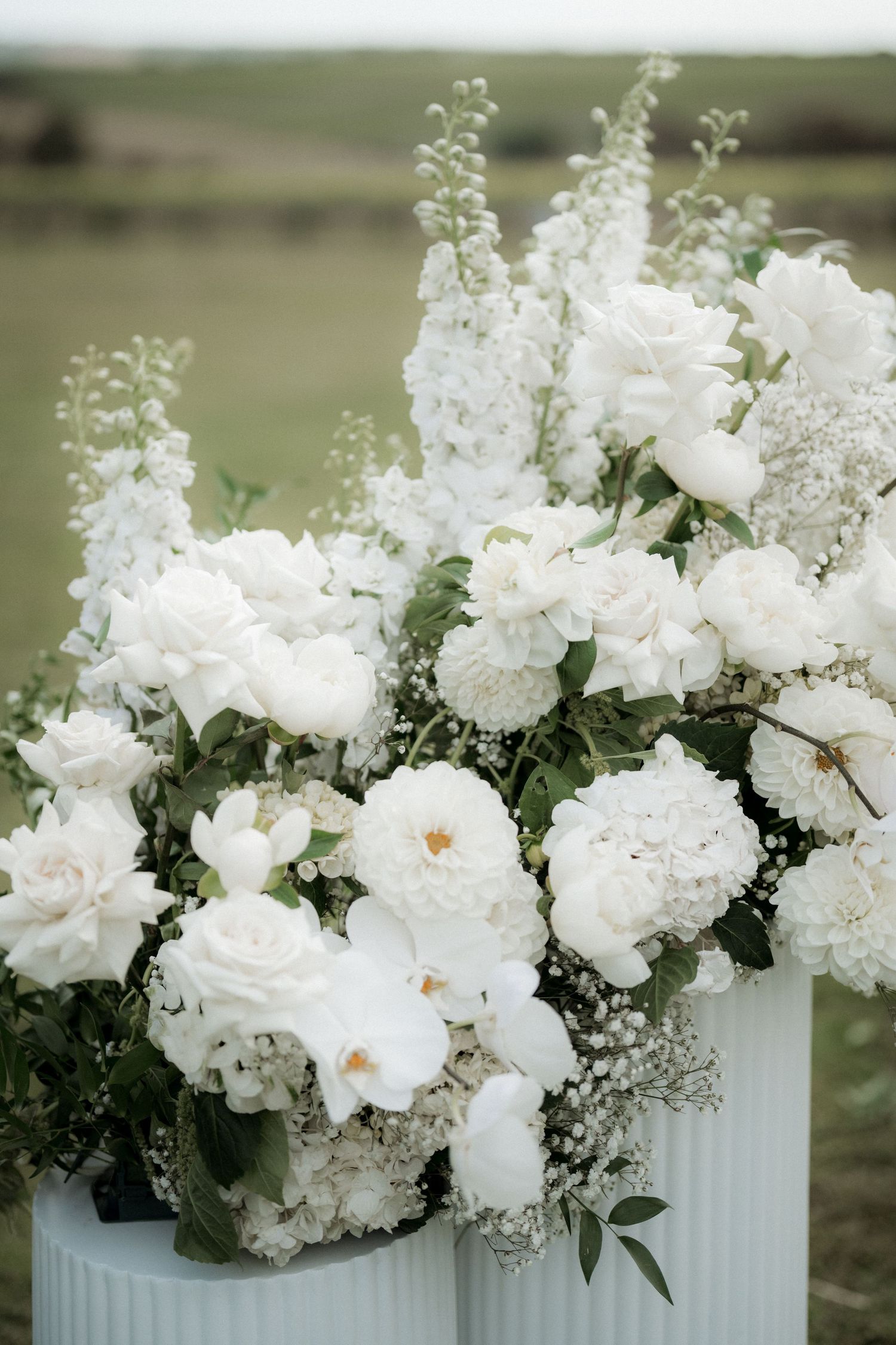 Elegant white floral arrangement with roses and delphinium in ribbed vases.