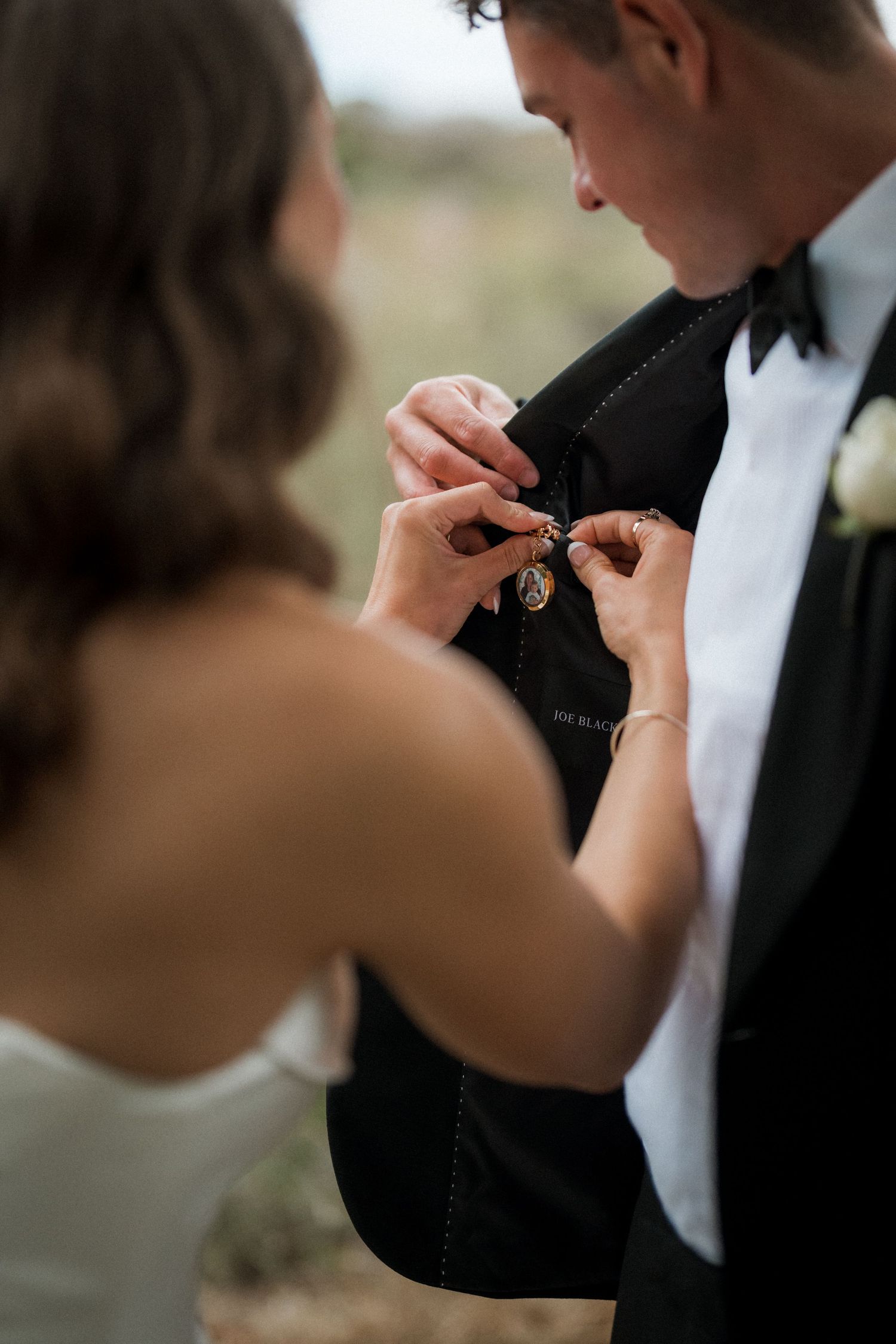 Close-up shot of hands pinning boutonniere on formal tuxedo.