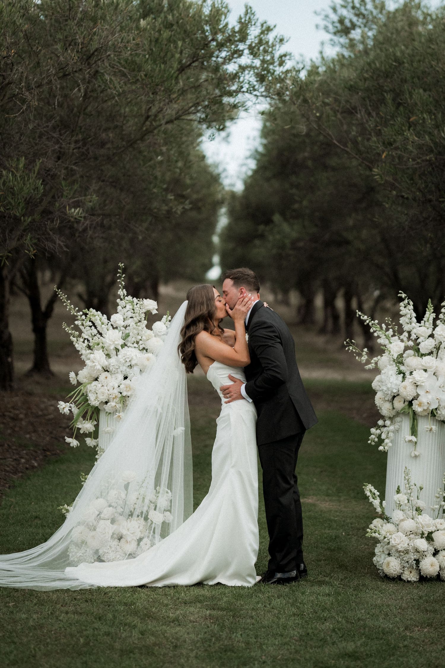 Elegant wedding ceremony setup with white floral arrangements in an olive grove.