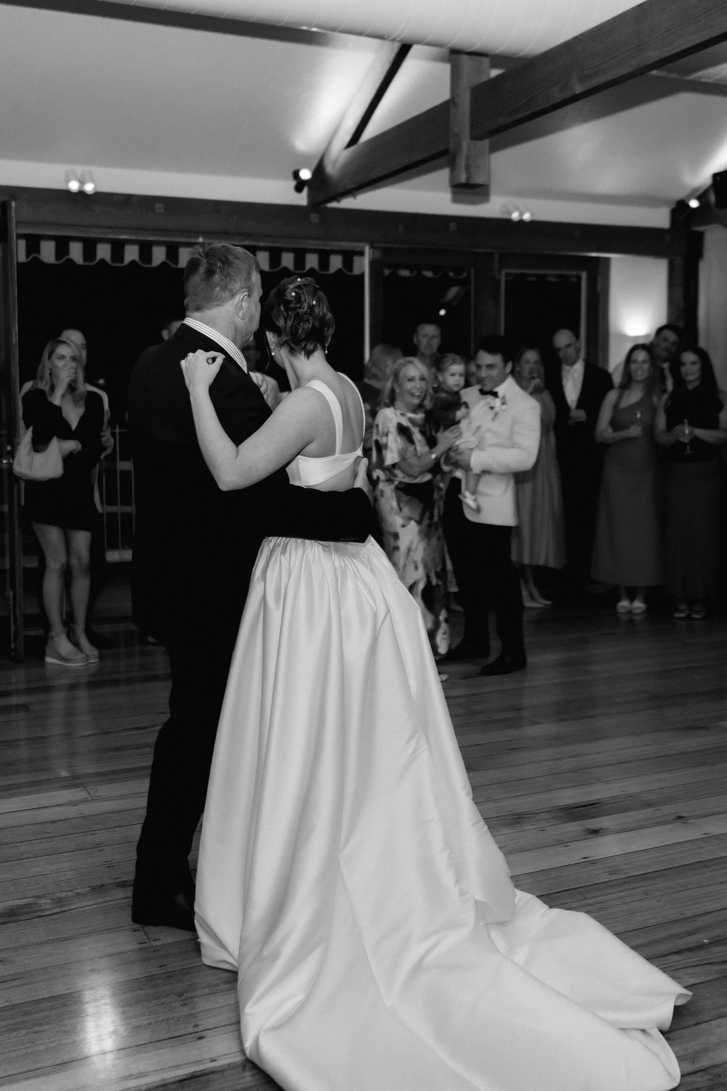 Wedding dance on hardwood floor with flowing white gown in black and white photography.