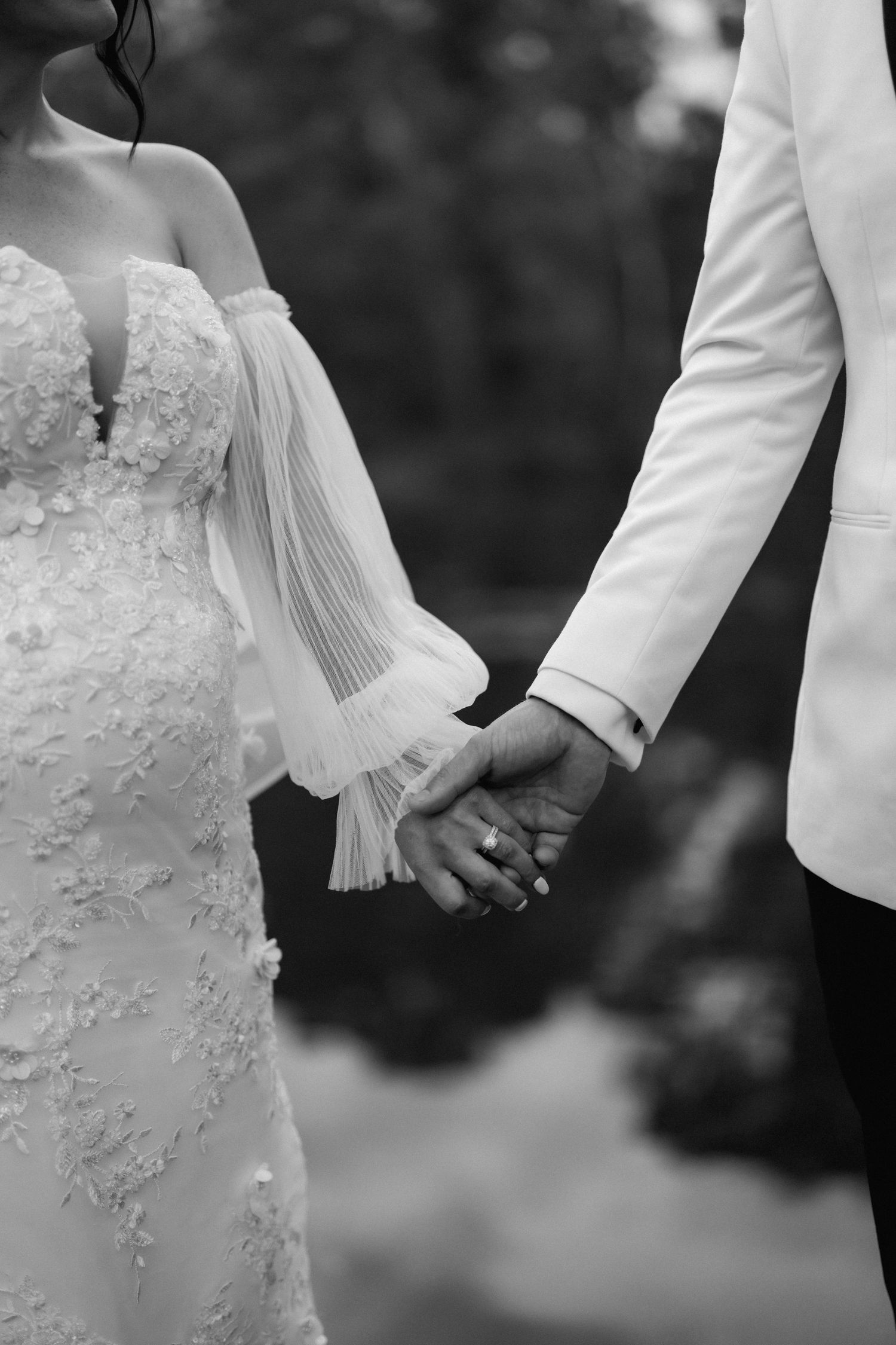 Black and white detail shot of couple holding hands showing wedding attire.