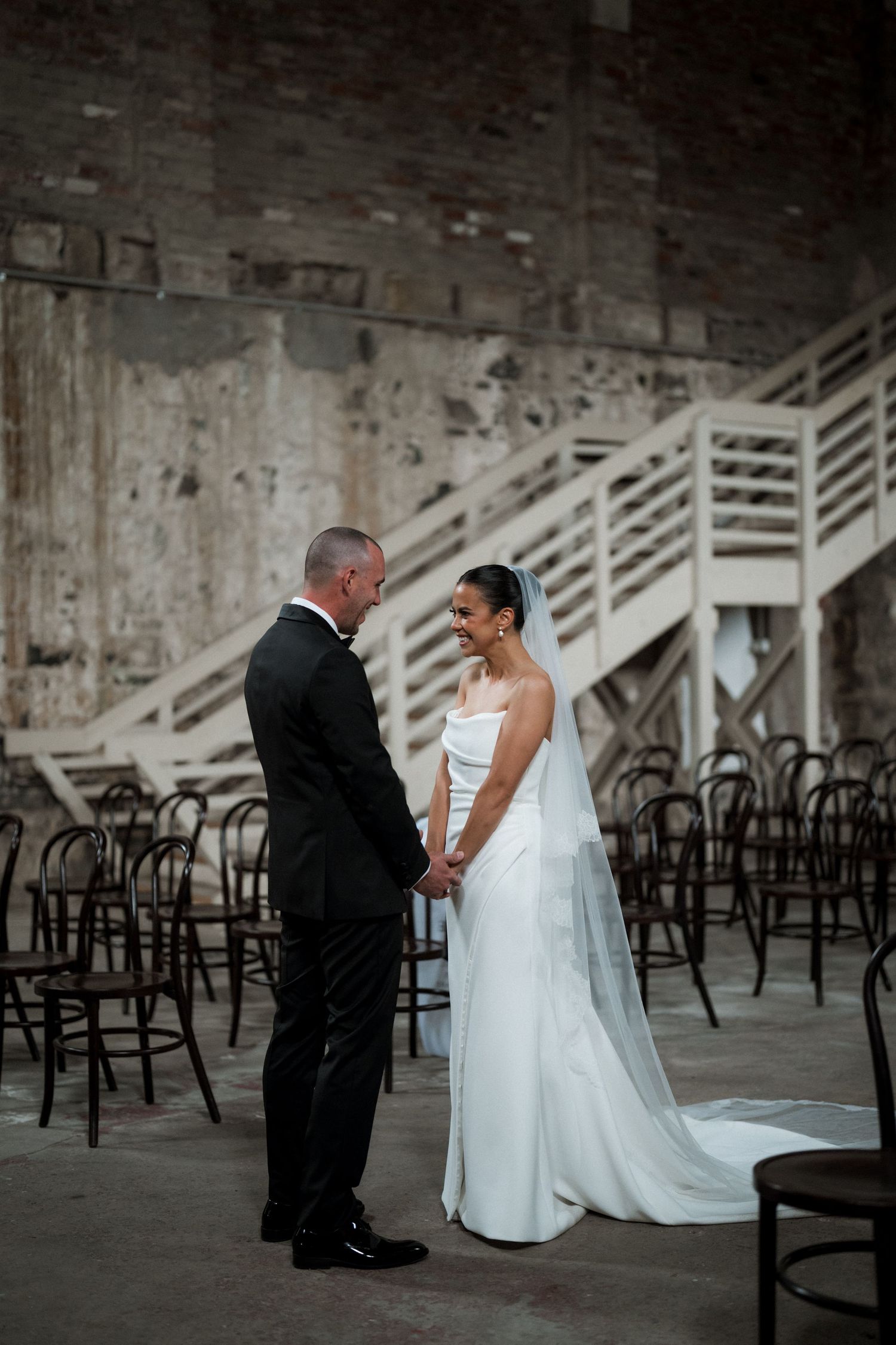 Wedding couple shares tender moments in historic brick venue with bentwood chairs.
