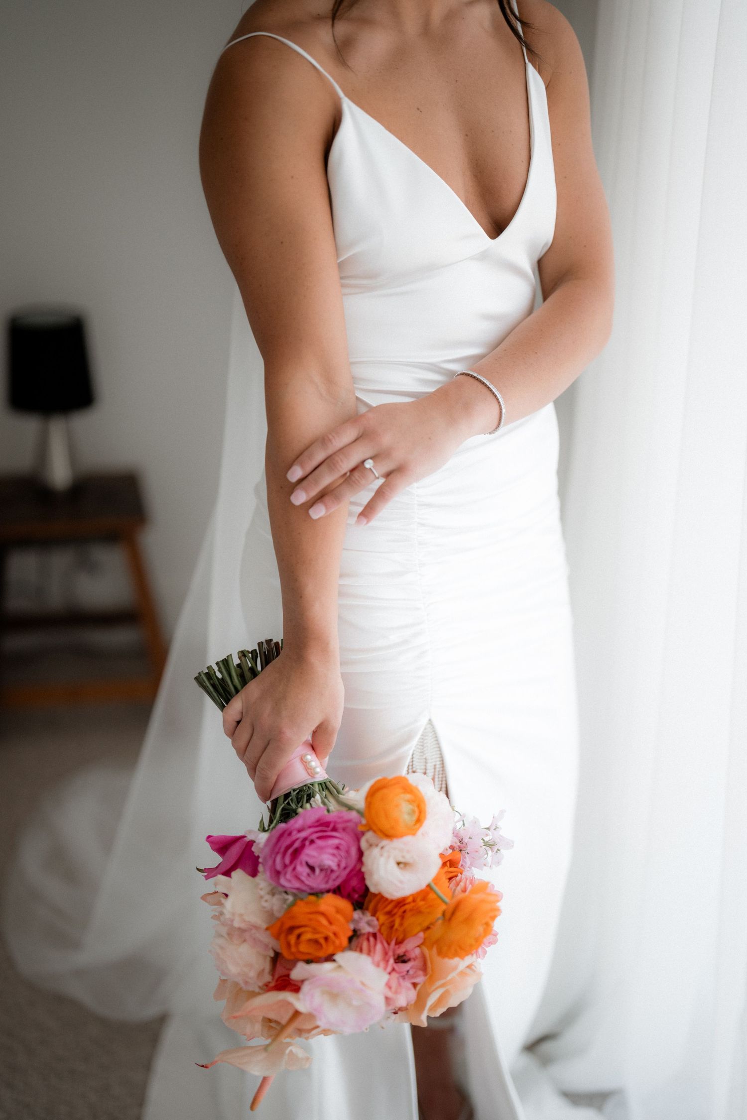Elegant bride in white dress holding a vibrant bouquet of pink and orange flowers.