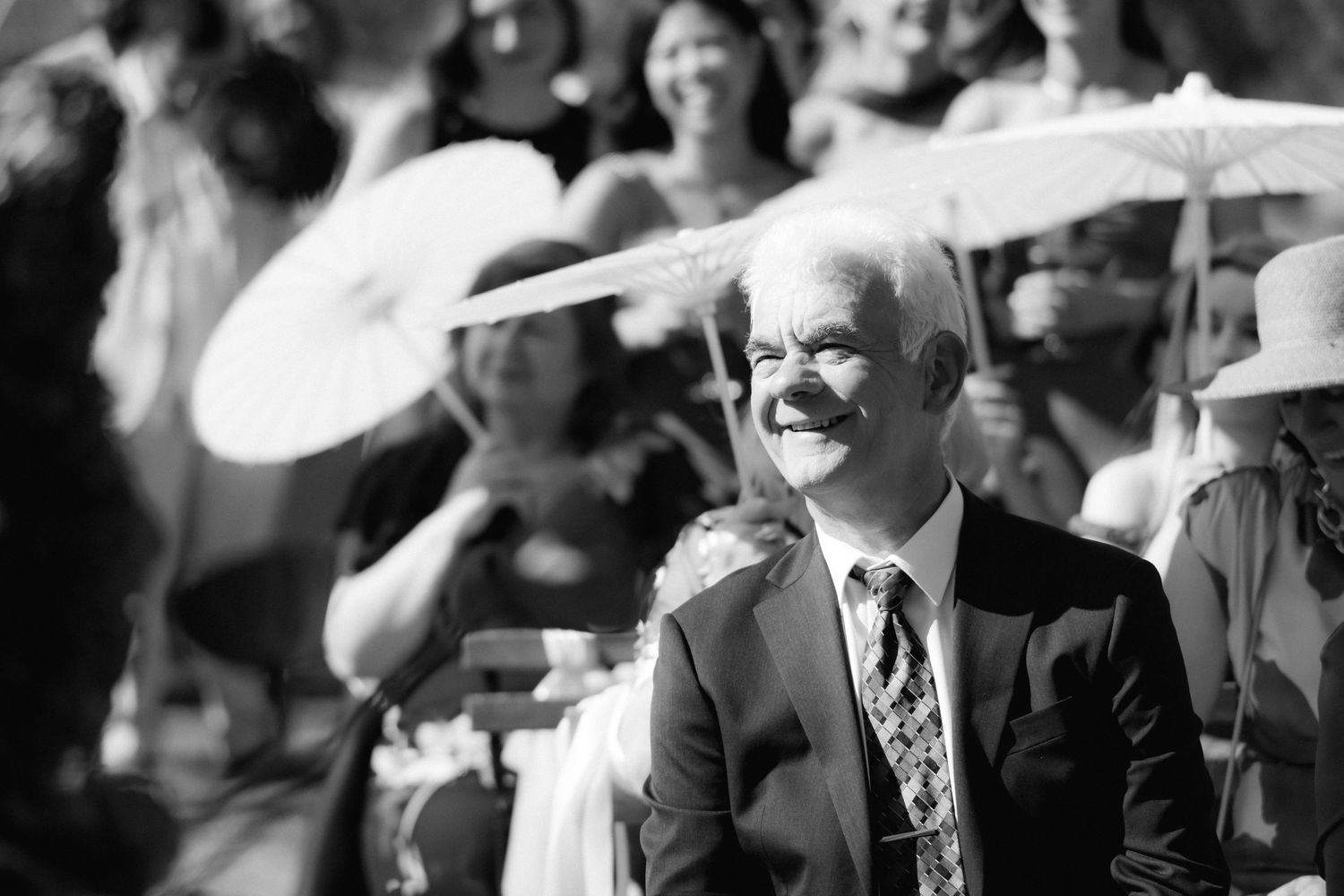 A black and white photograph shows spectators at a formal event wearing suits and hats looking upward.