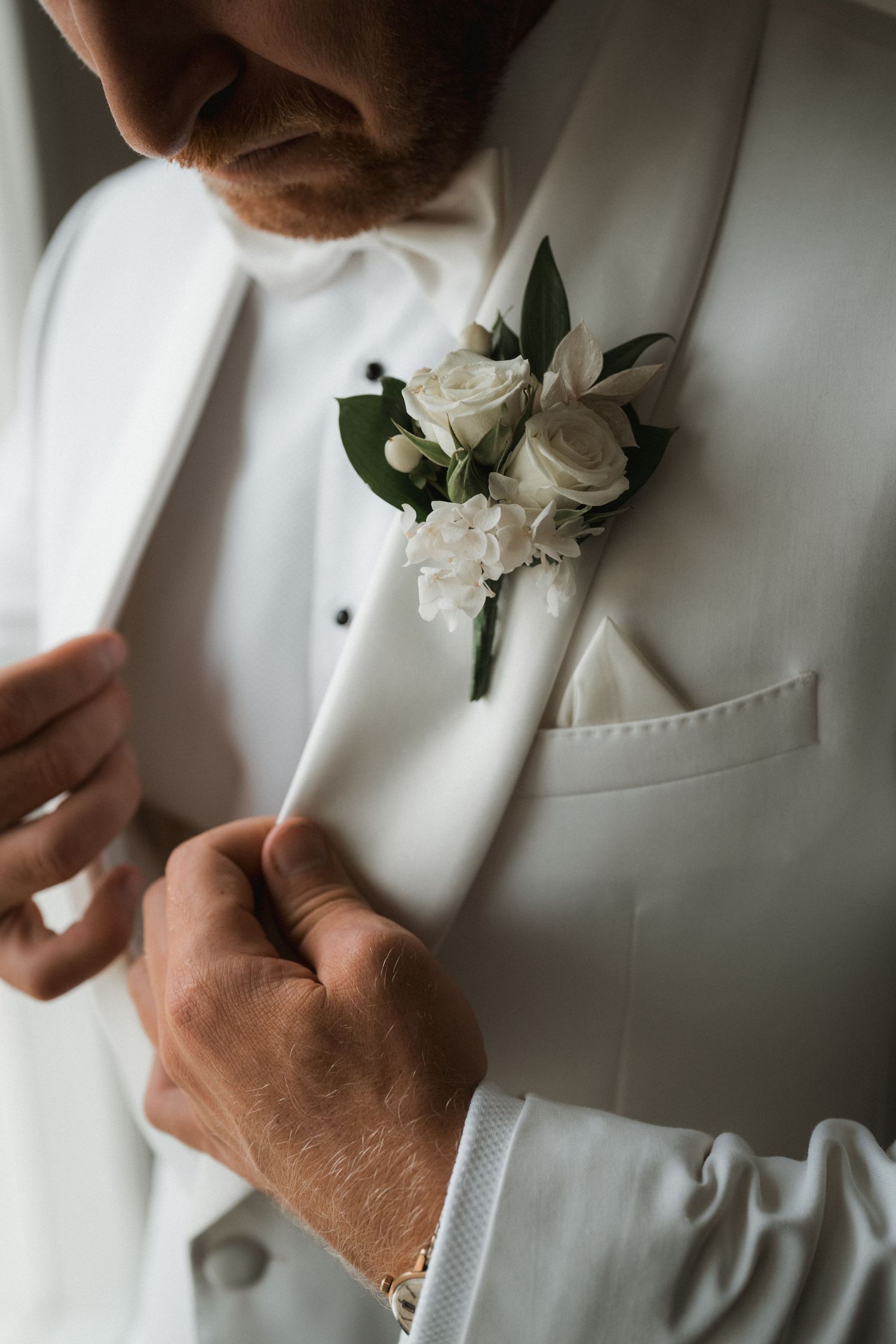 Close-up of a white boutonniere with roses pinned to a formal white tuxedo jacket lapel.