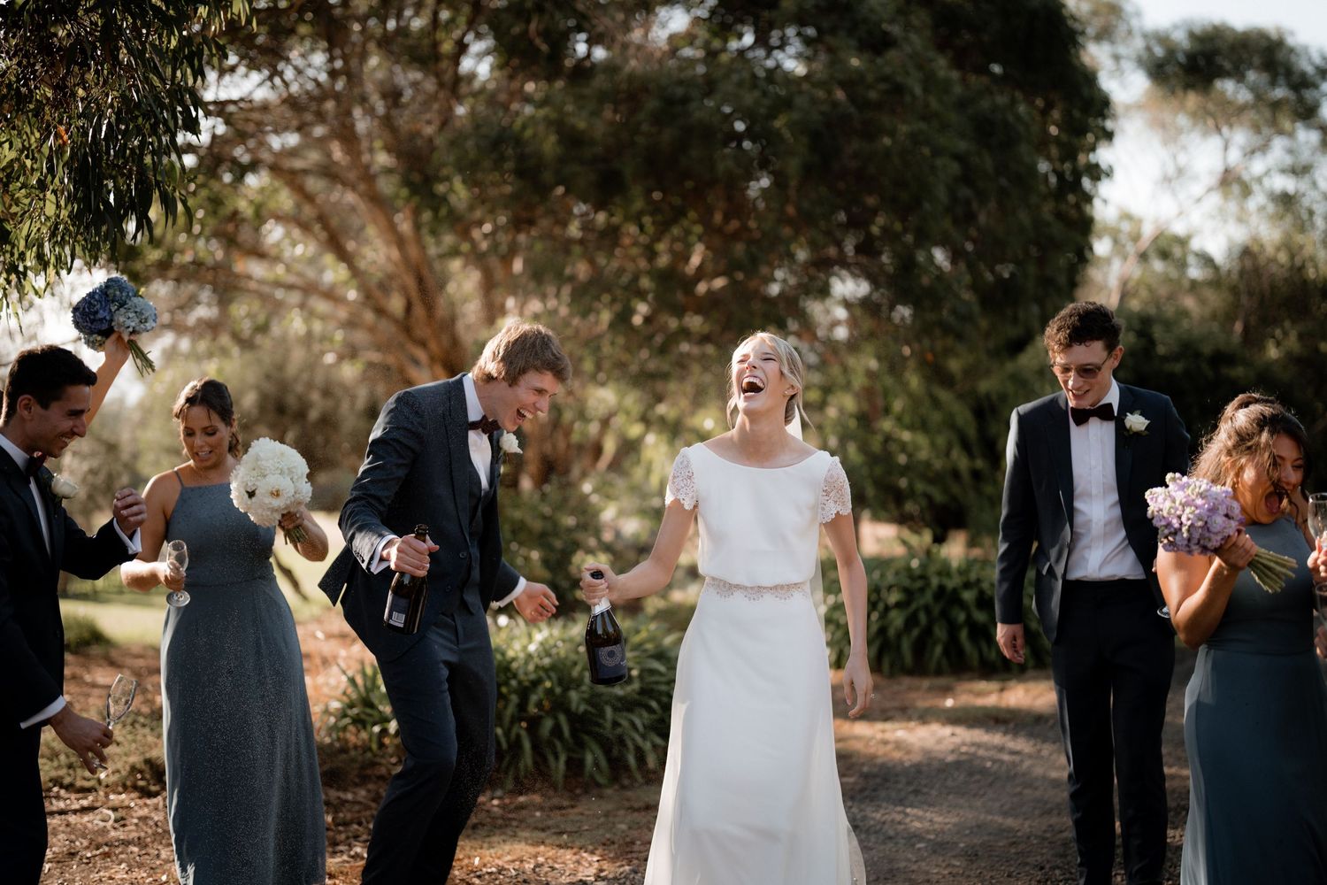 Wedding celebration outdoors with wedding party in formal attire among trees.