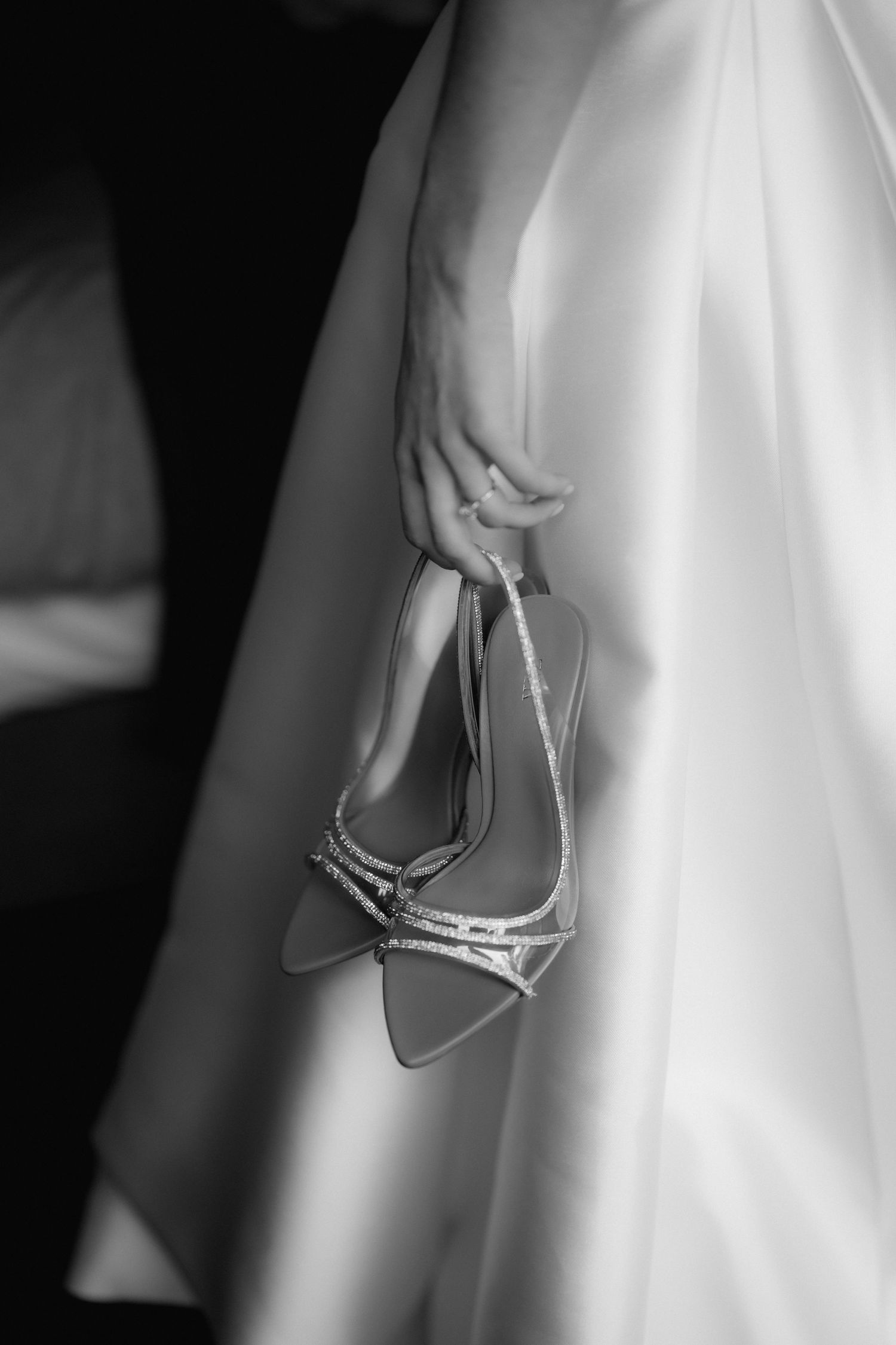Close-up black and white photo of sparkly bridal shoes held against wedding dress.