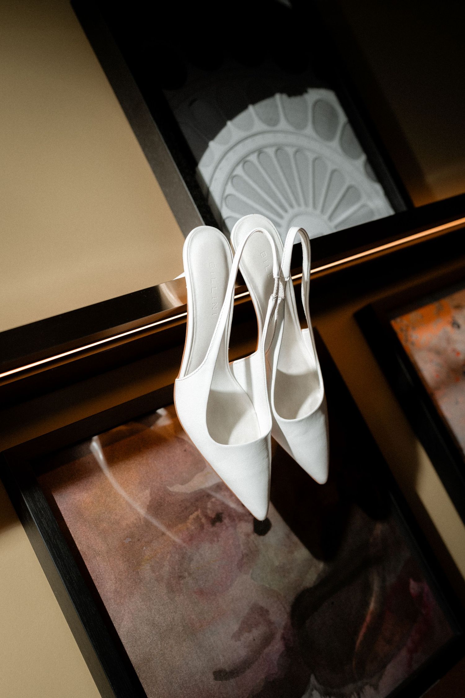 Elegant white slingback heels displayed against a dark background with decorative architectural details.
