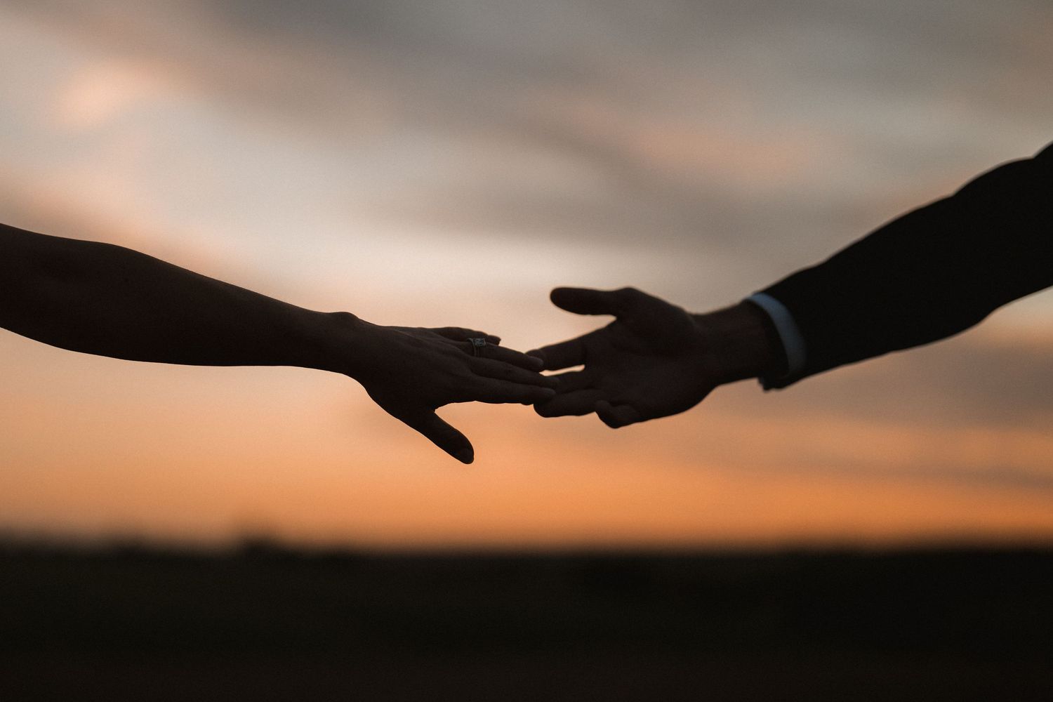 Silhouette of hands reaching for each other against sunset sky.