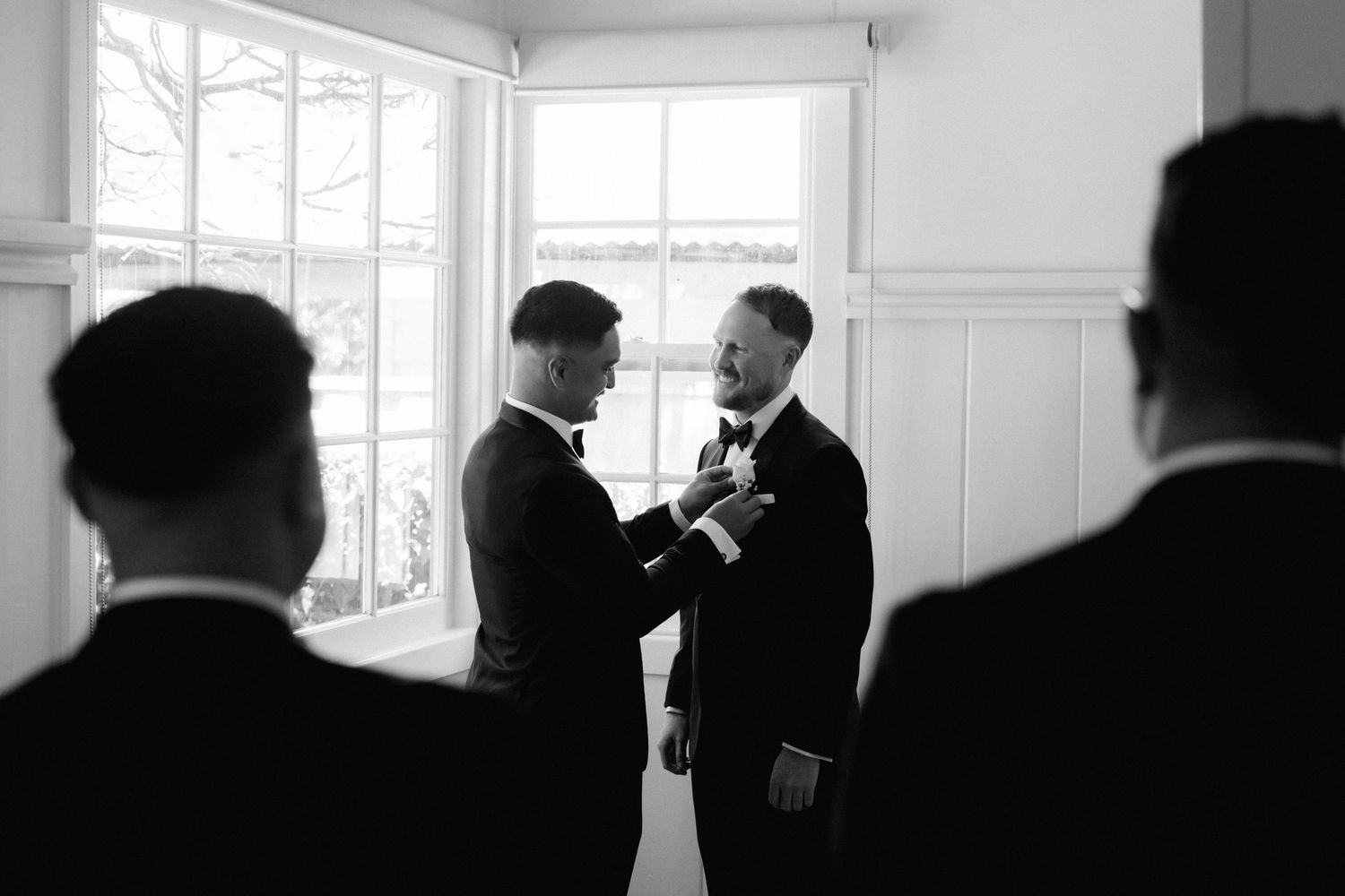 Groomsmen in black suits sharing a candid moment together before the wedding ceremony.