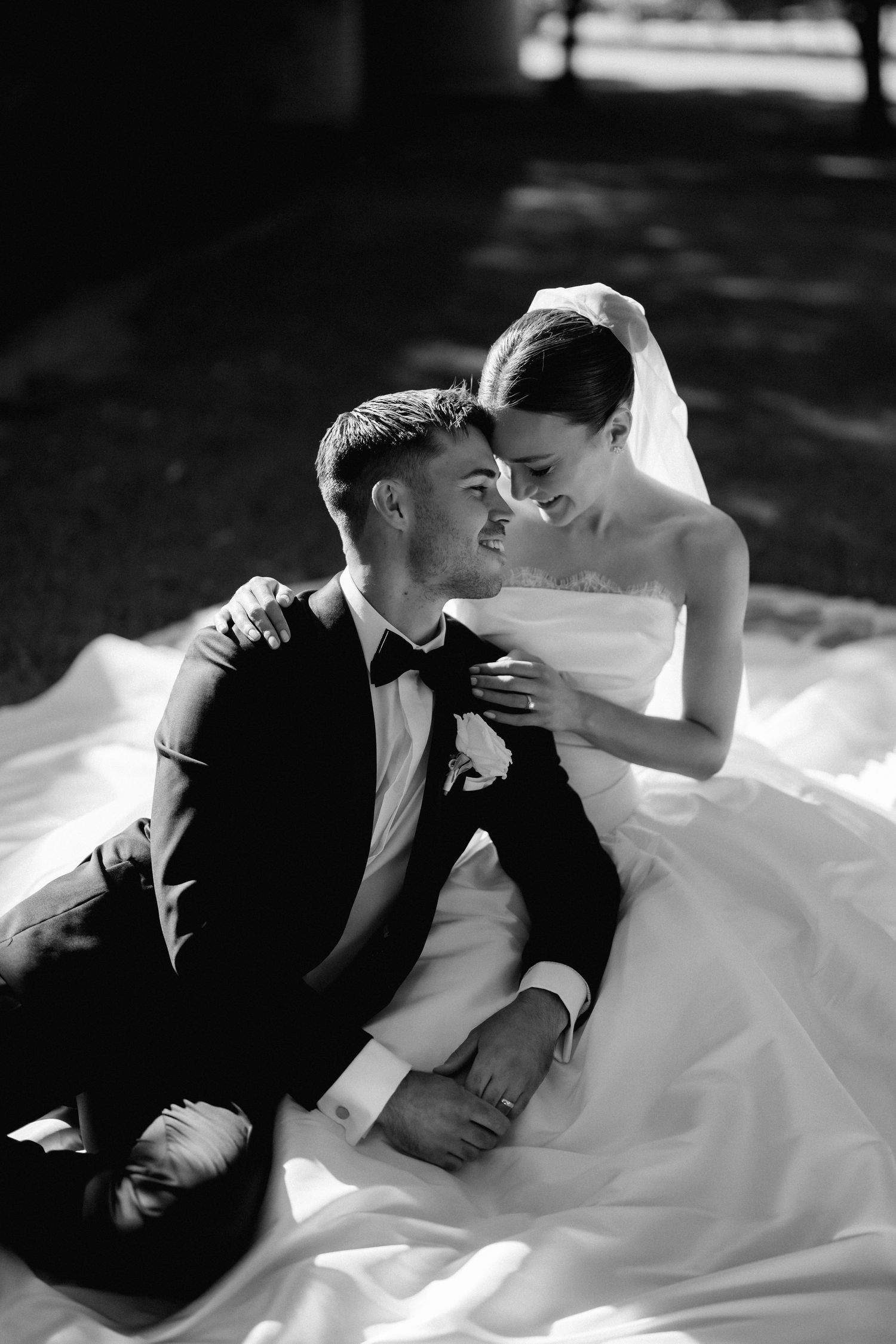 Romantic black and white portrait of a couple lying on grass in wedding attire.