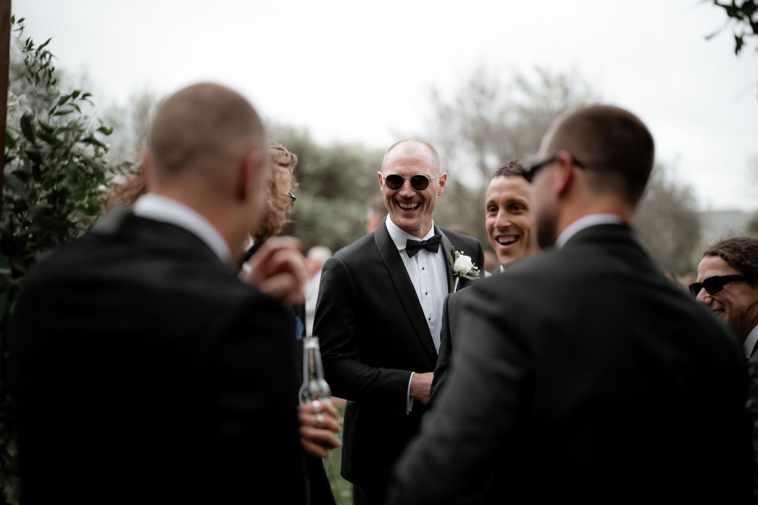 A group enjoying drinks and laughter during an outdoor wedding celebration.