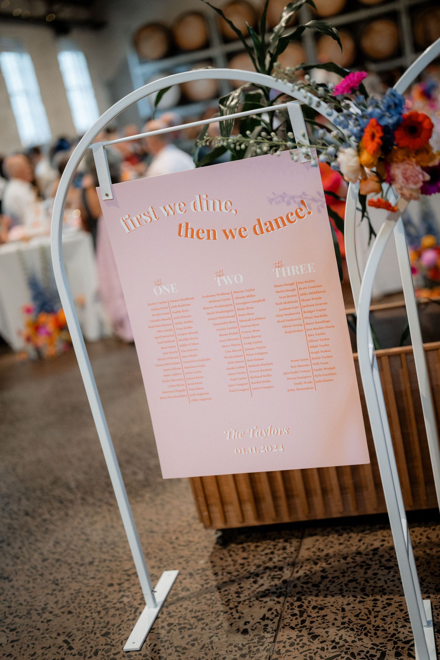 Pink seating chart display with gold lettering mounted on white metal stands.