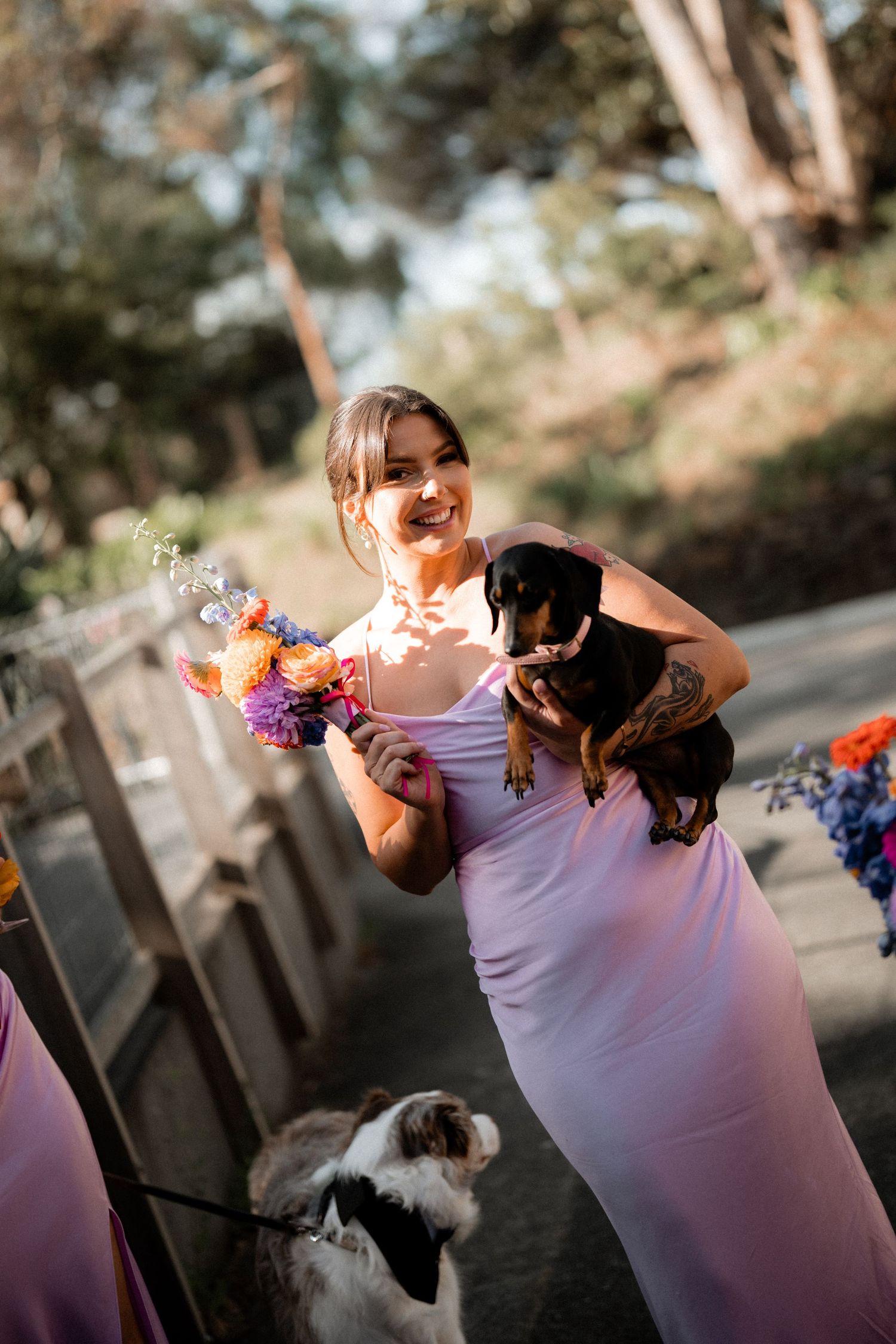 Bridesmaid in lavender dress adjusting colorful floral corsage in outdoor setting.