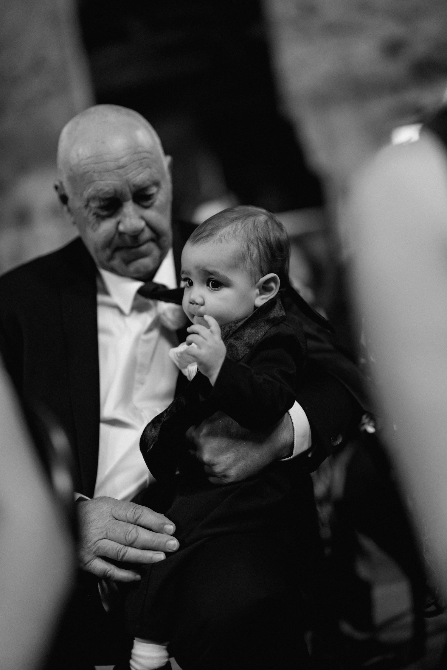 Tender black and white portrait of a small baby being held during formal event.