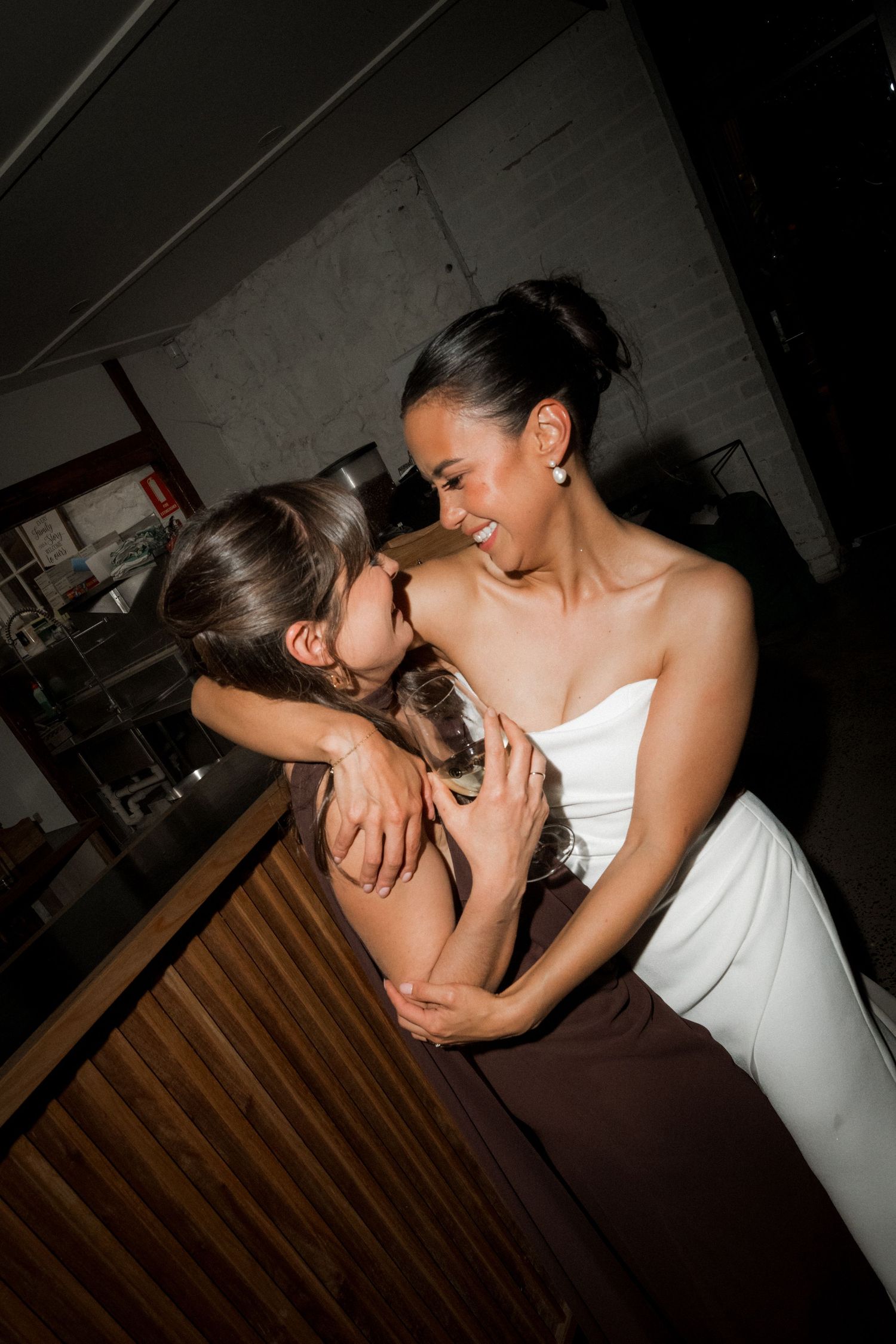 Two people in white dresses share an intimate moment during what appears to be a wedding celebration.