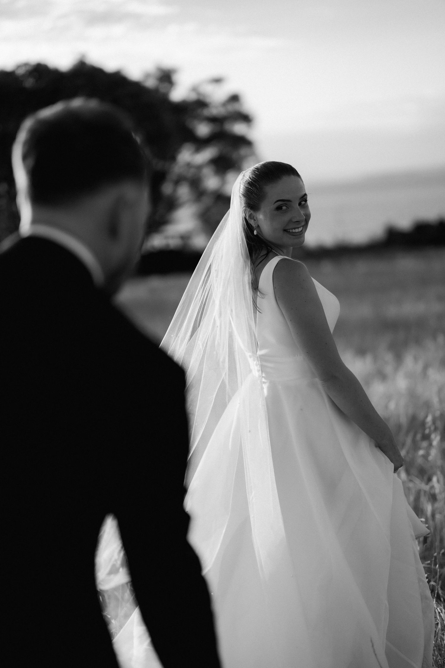 A black and white wedding photo series showing candid moments between a bride in flowing veil and groom in an outdoor field.