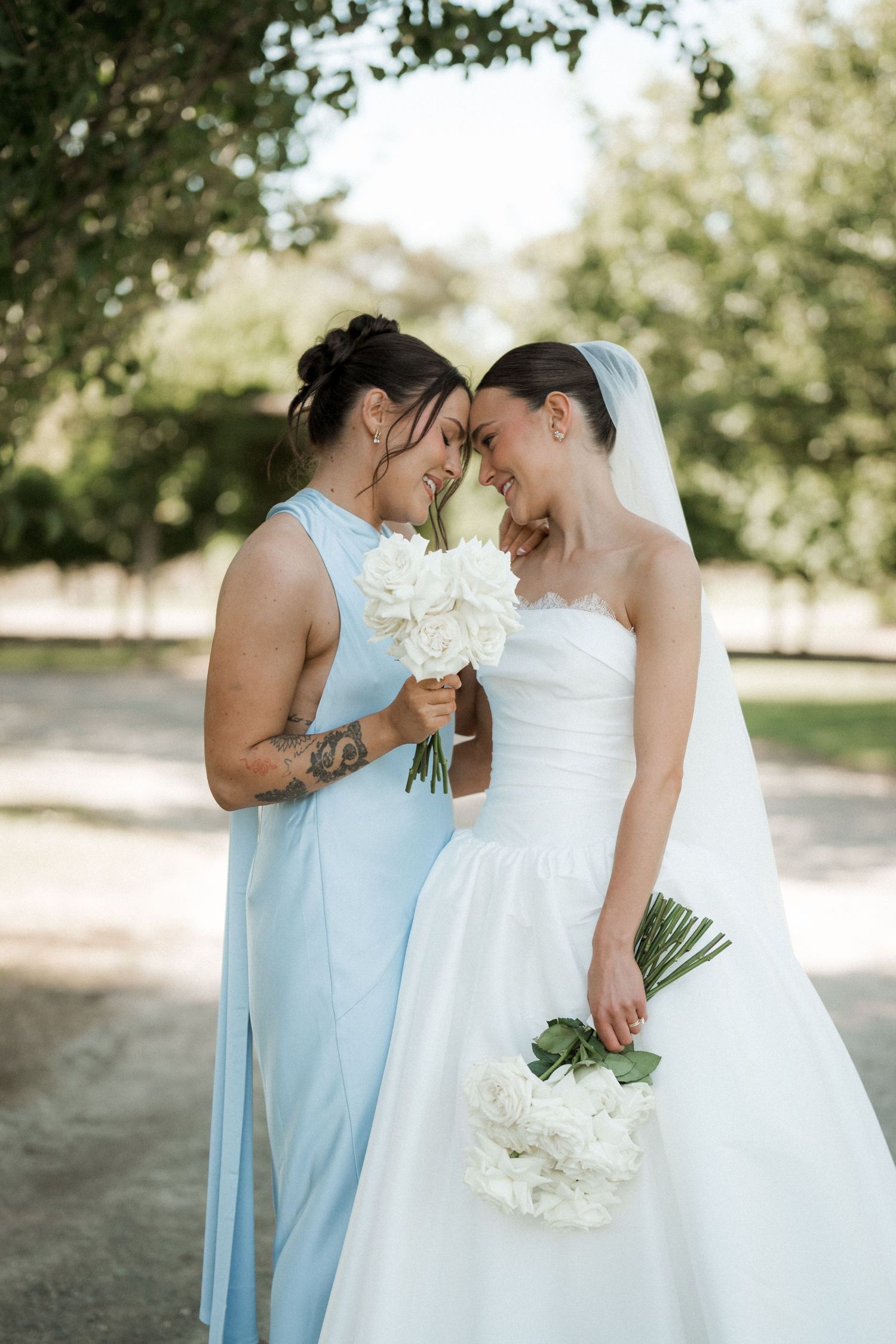 Two people in wedding attire share an intimate moment while holding white bouquets.