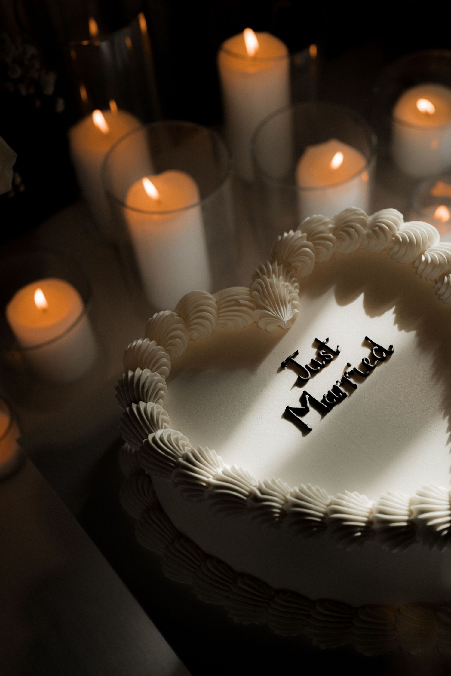 White wedding cake with lit candles creating dramatic shadows in dark setting.