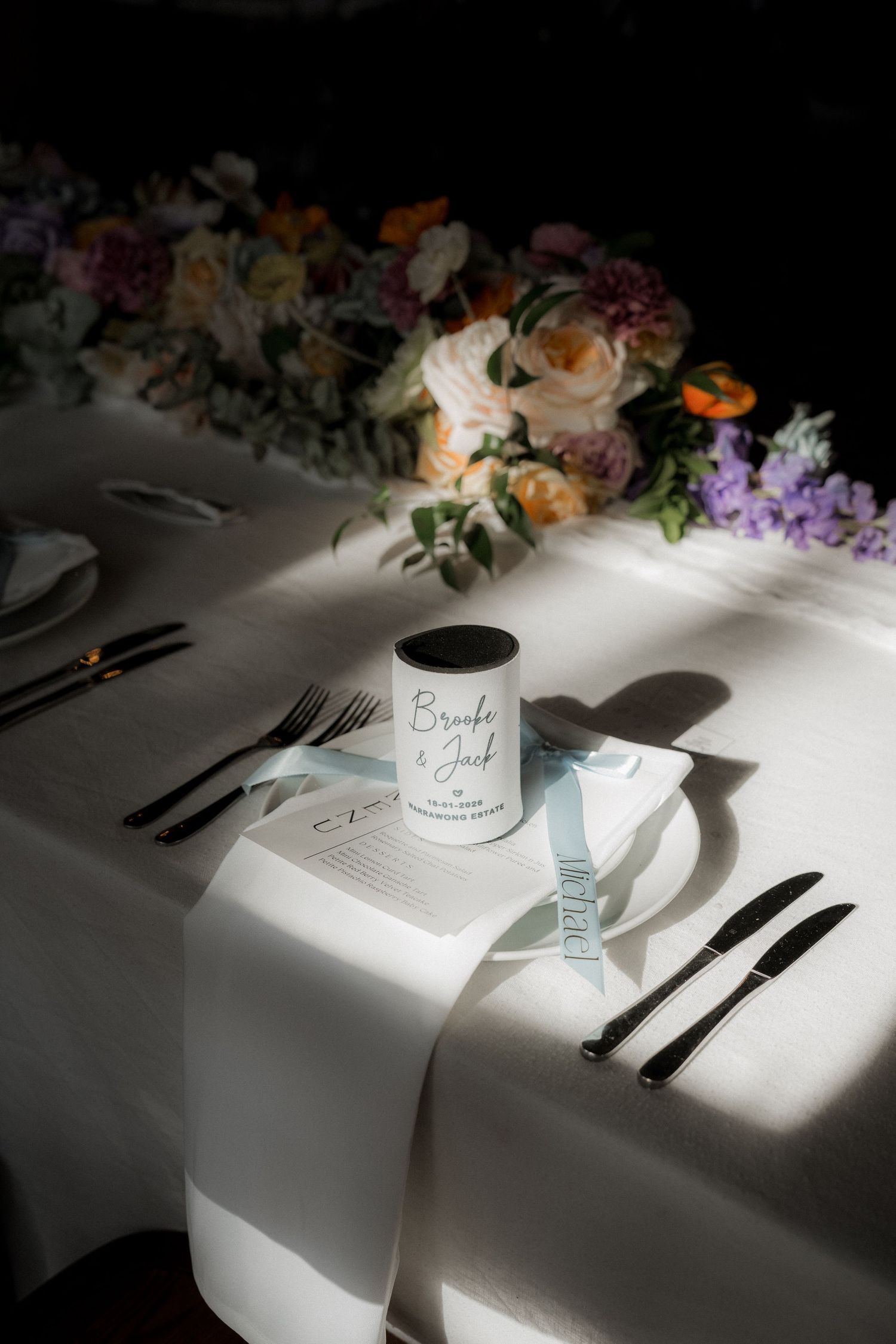 Elegant wedding table setting with floral centerpiece and personalized Brooke and Jack candle favor.